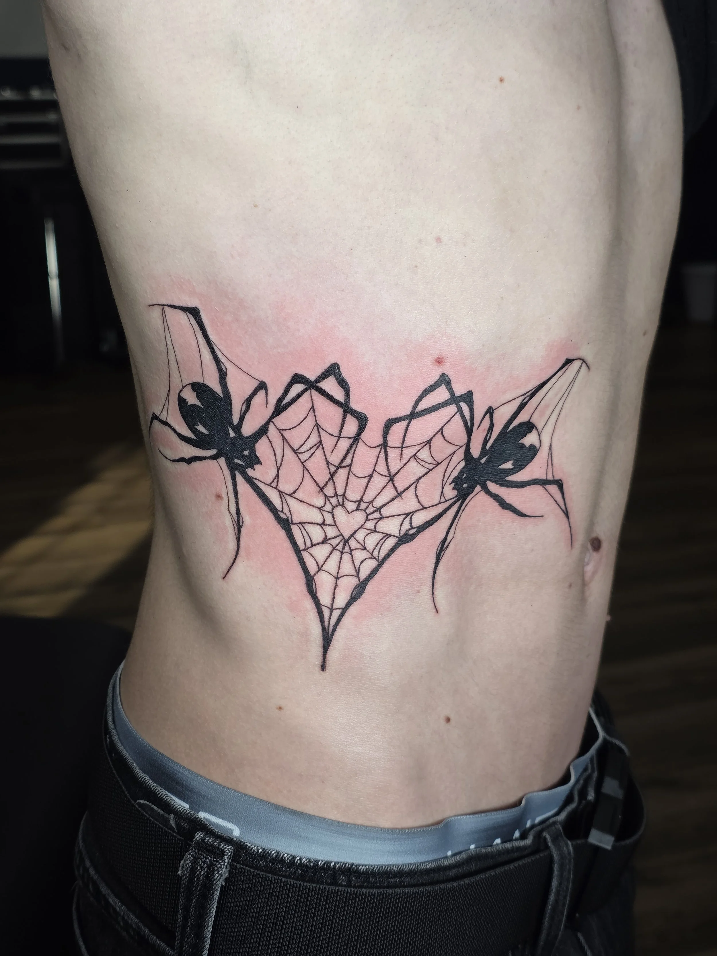 Tattoo of a spider on a person's side, with web design and a heart in the center.
