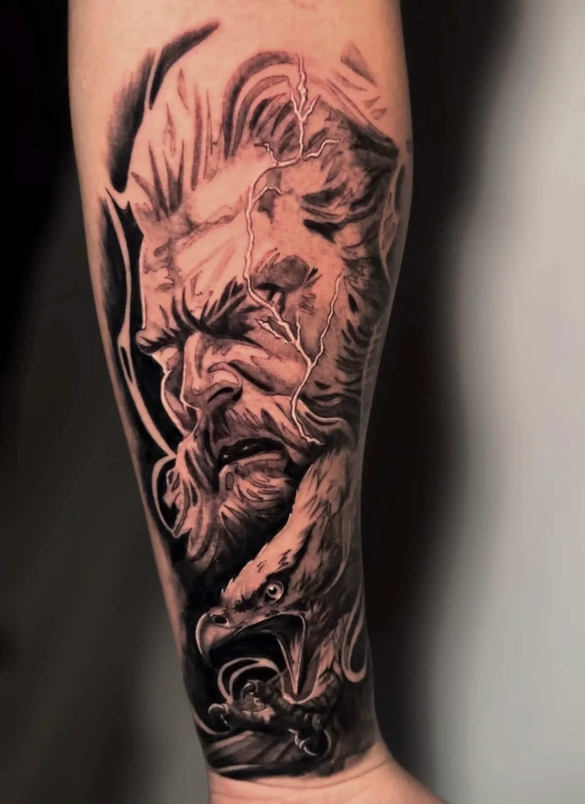 Black and gray tattoo of a man's face and a bird's head, with lightning bolts connecting them, on a person's arm.