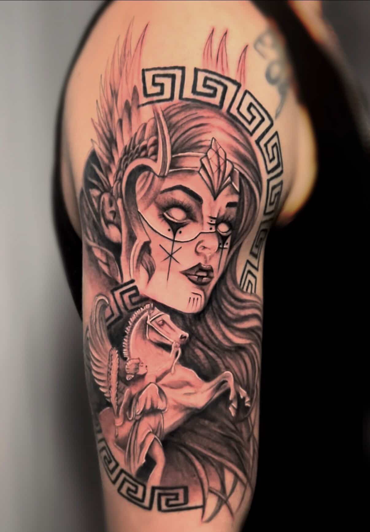 Black and gray tattoo of a woman with an elaborate headpiece, mysterious eye makeup, and a stylized face, surrounded by geometric patterns and a horse's head at the bottom.
