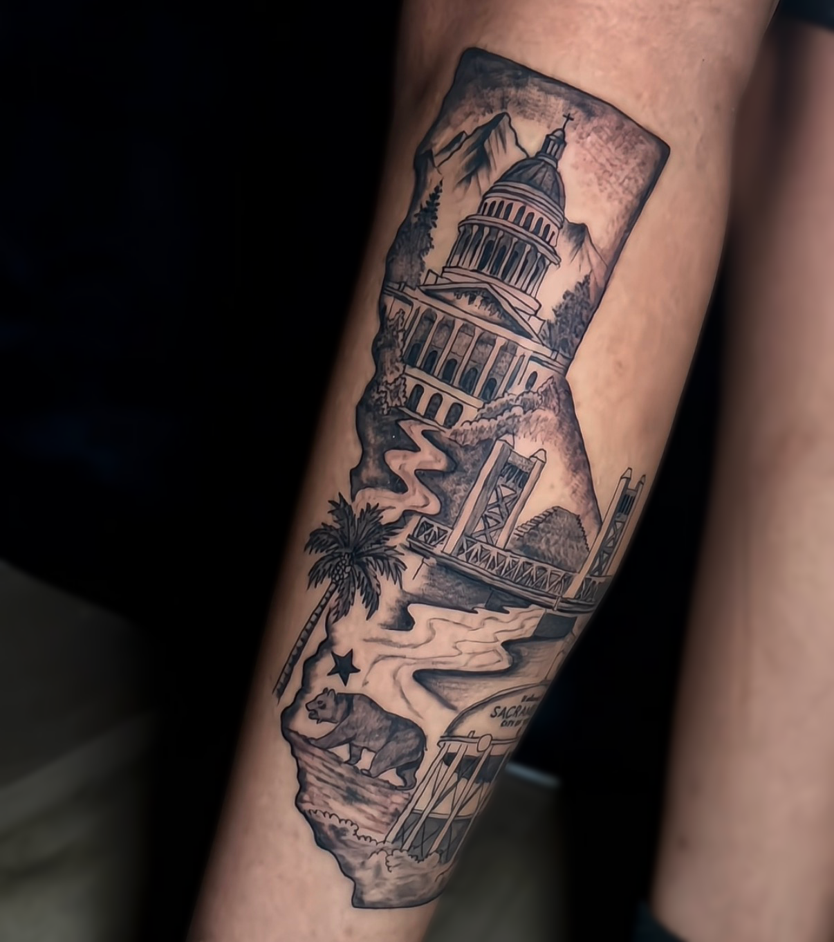 Tattoo of California landmarks including the Capitol building, Golden Gate Bridge, palm tree, mountain, star, bear, and water scene.