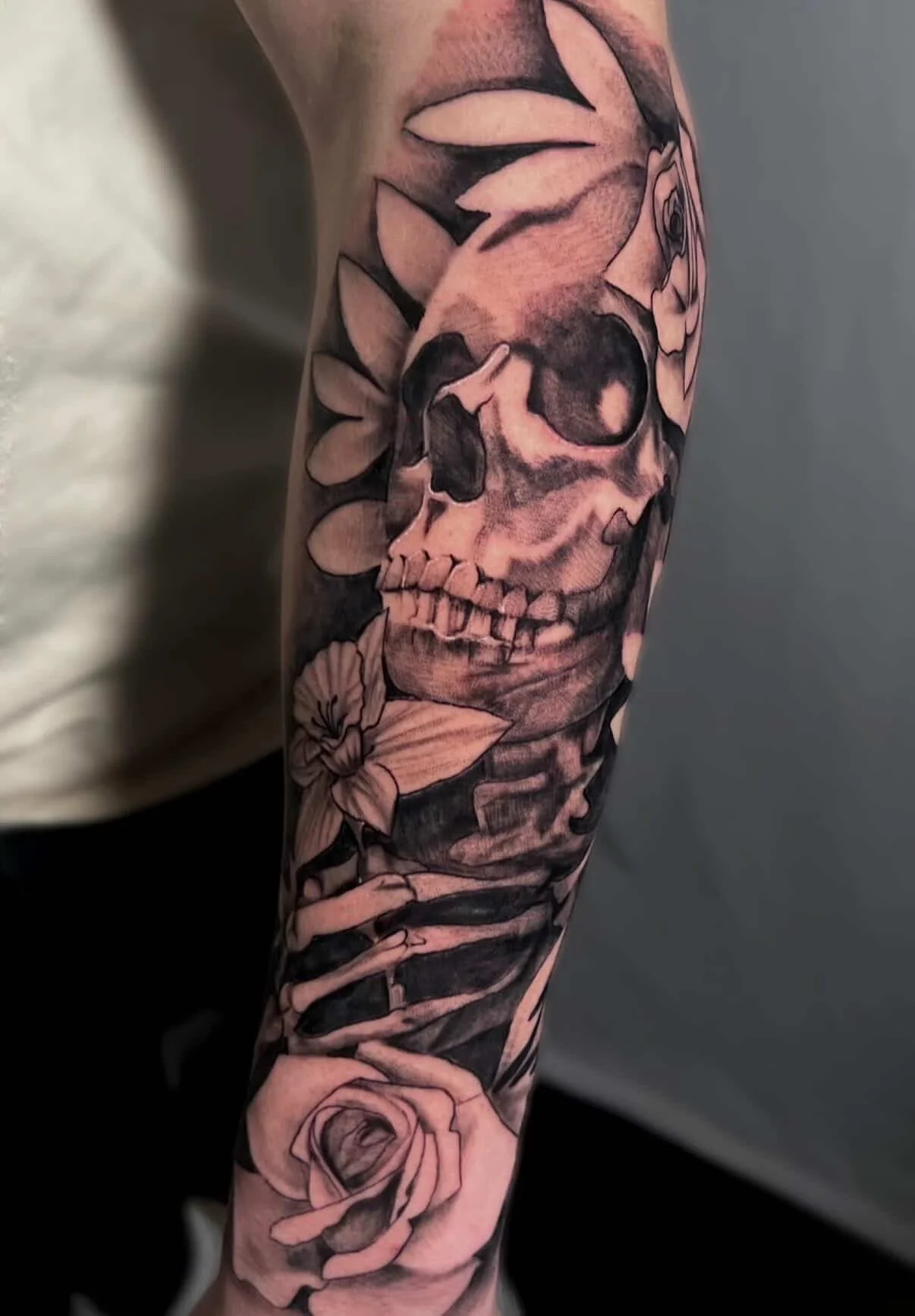 Tattoo of a skull, rose, and flowers on a person's arm.