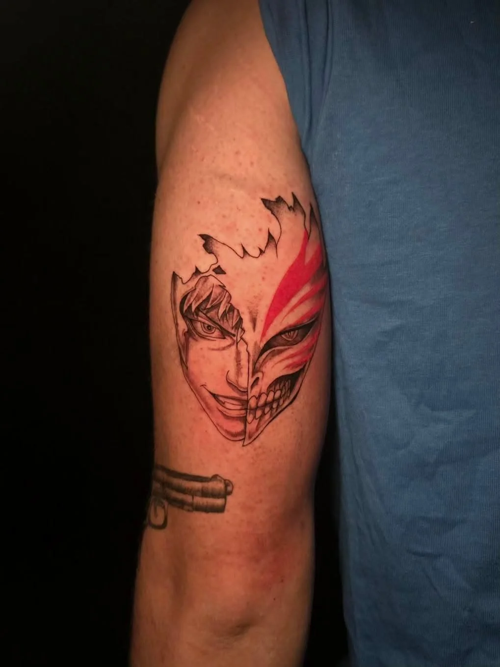 Tattoo of a split face, part human smiling with glasses, part graffiti-style skull, on a person's upper arm.
