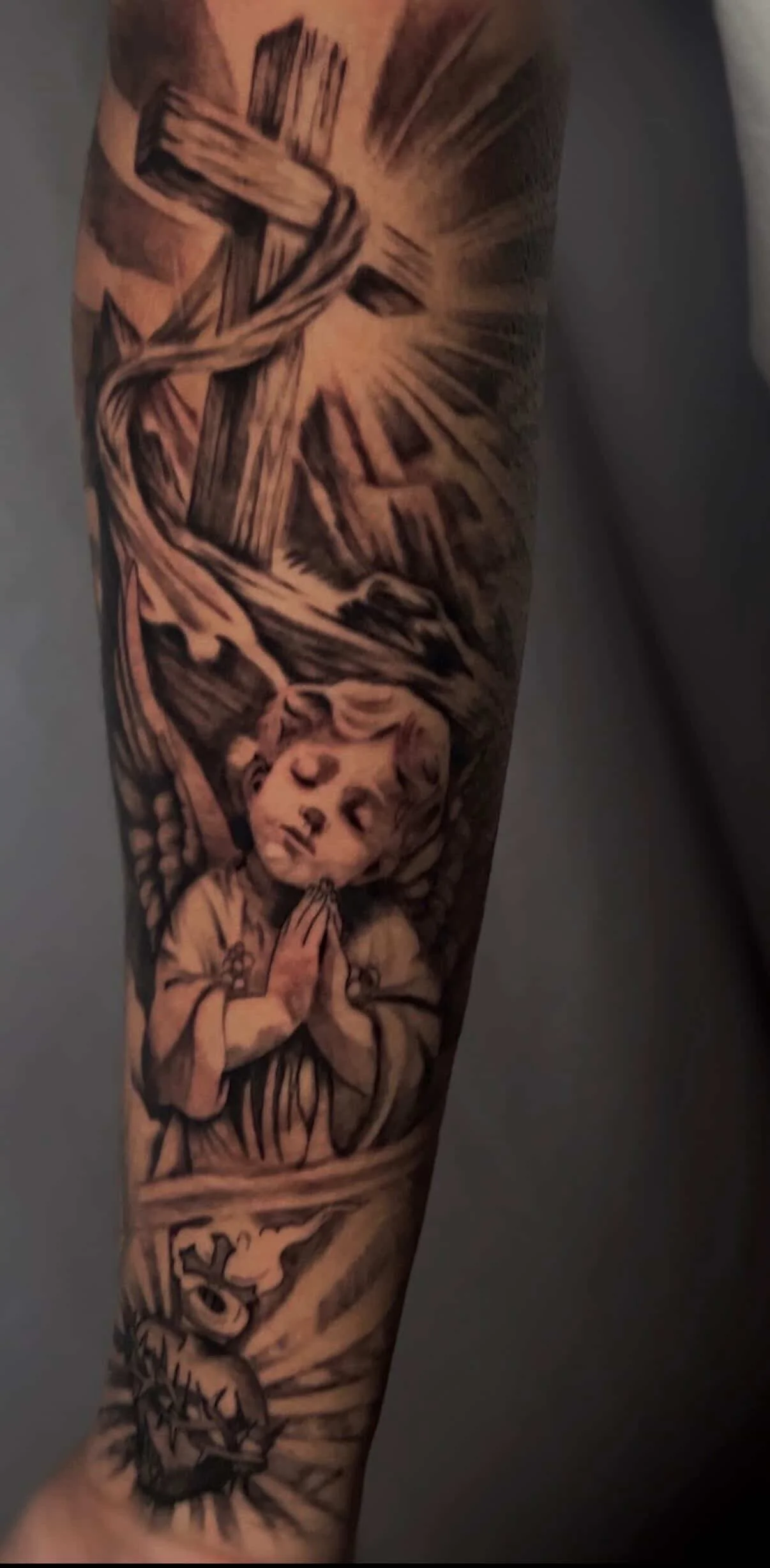 Tattoo of a praying child with hands together, angels wings, and rays of light emanating behind.