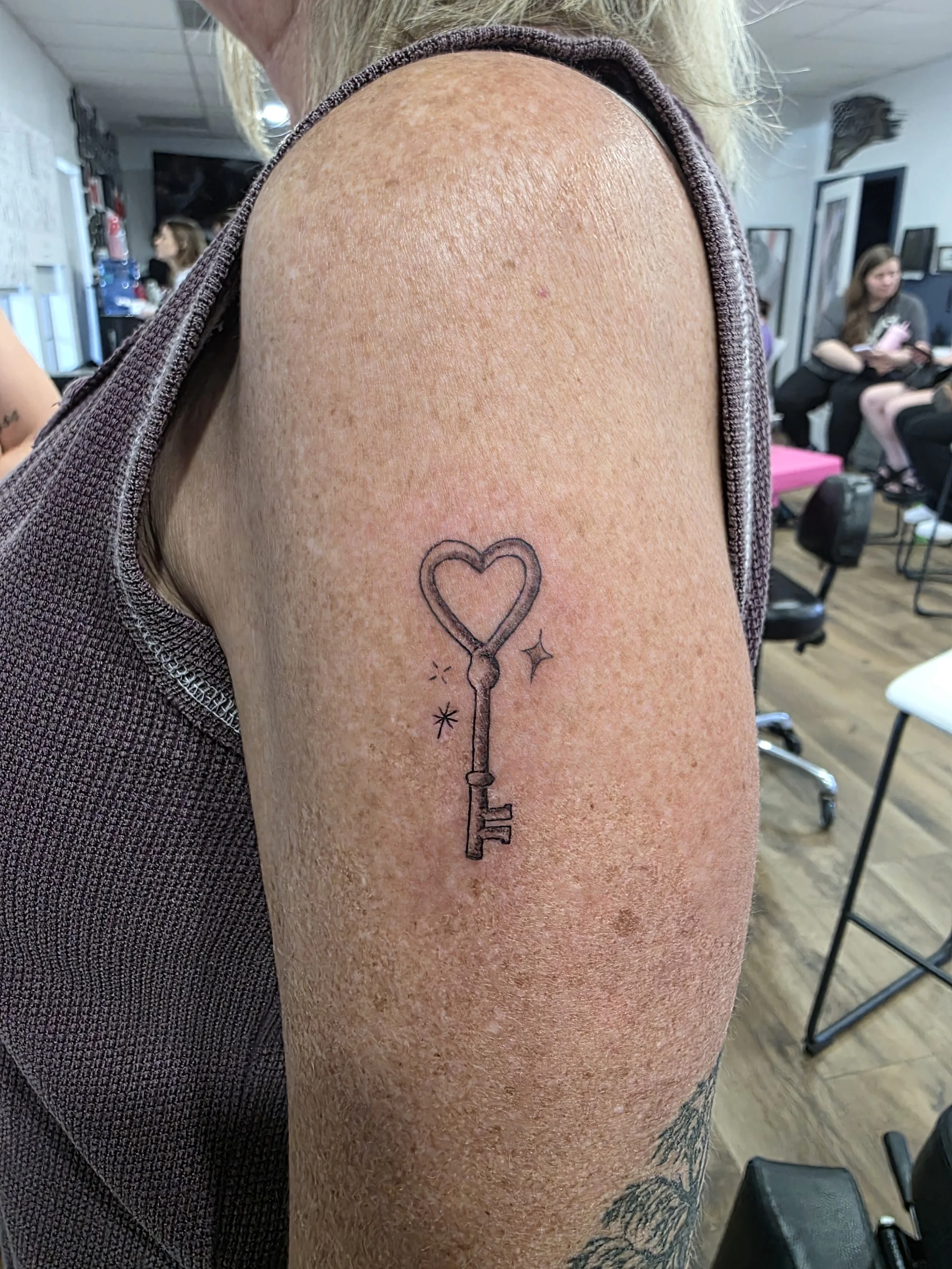 Tattoo of a key with a heart-shaped top on a person's upper arm.