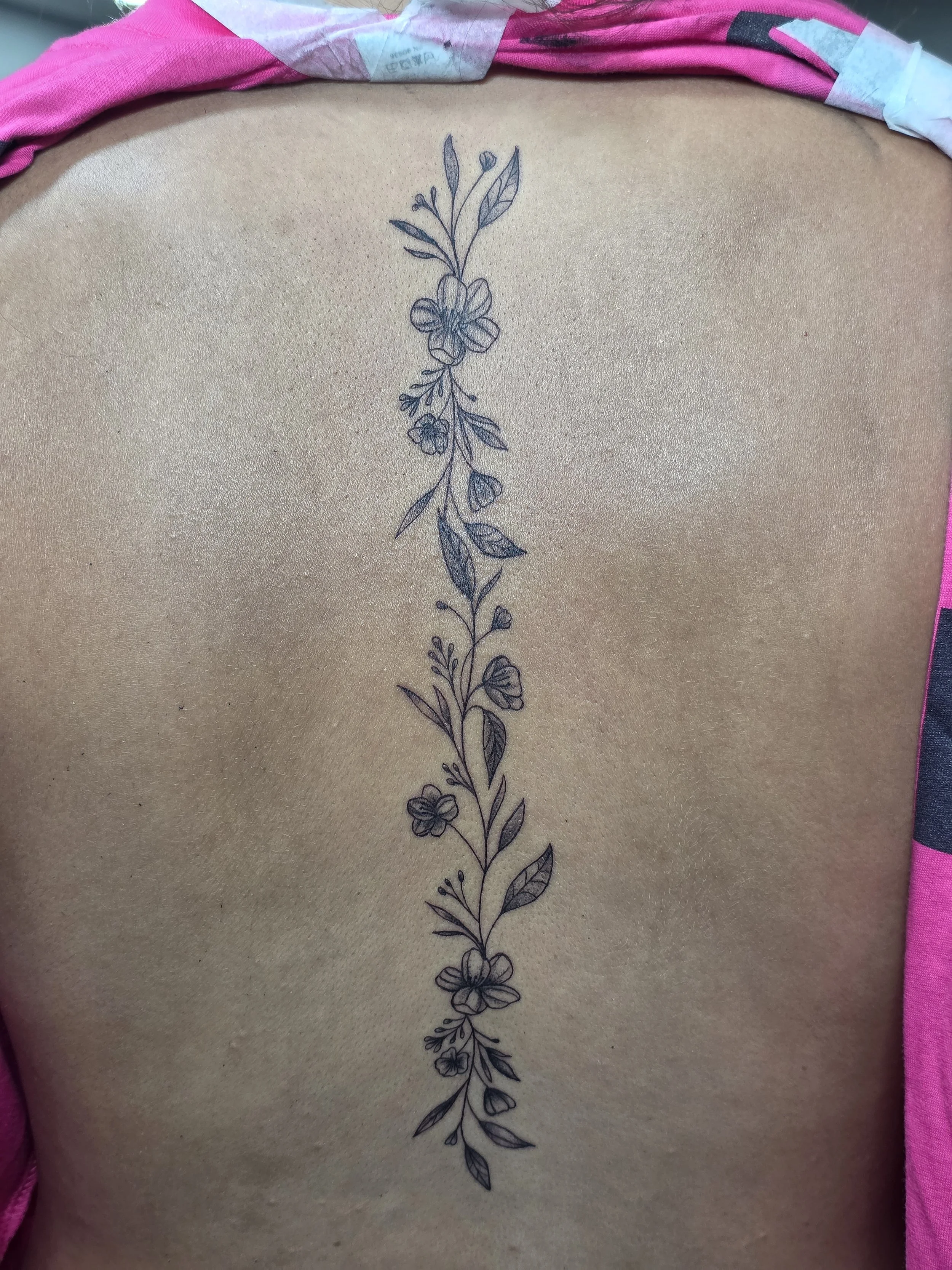 A vertical floral tattoo on someone's back featuring a bouquet of flowers and leaves.