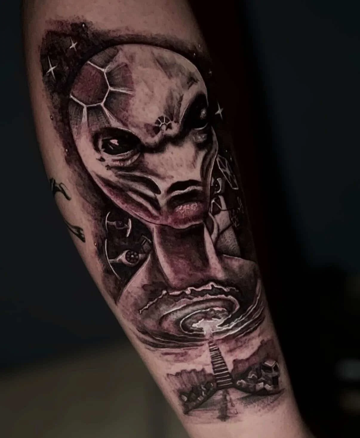 A detailed black and gray tattoo of a face with ocean waves, a celestial geometric pattern, and staircases on the forearm.