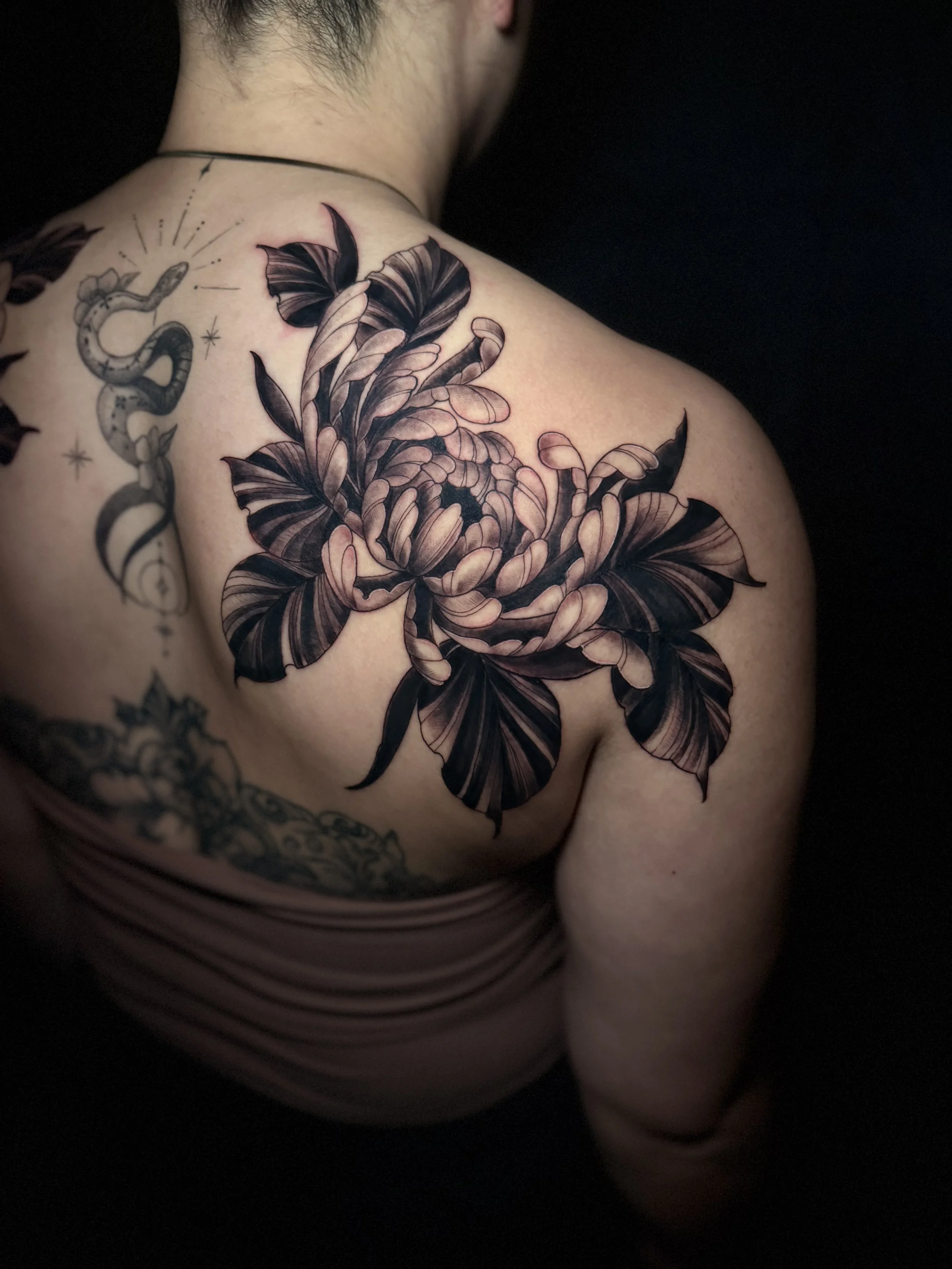 Close-up of a person's upper back and shoulder with a detailed tattoo of a large flower and butterfly among leaves.