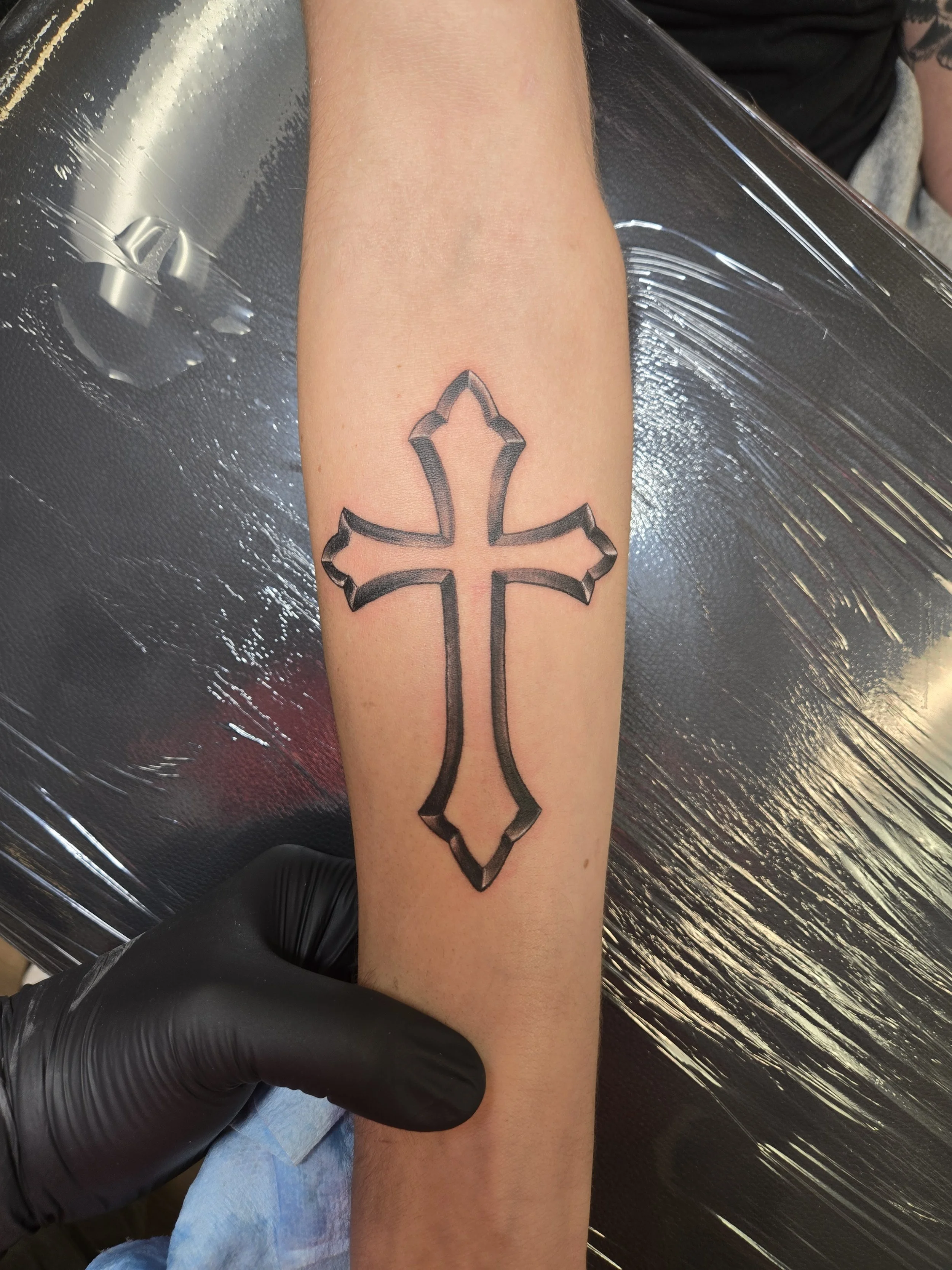 A tattoo of a stylized black cross on a person's arm.