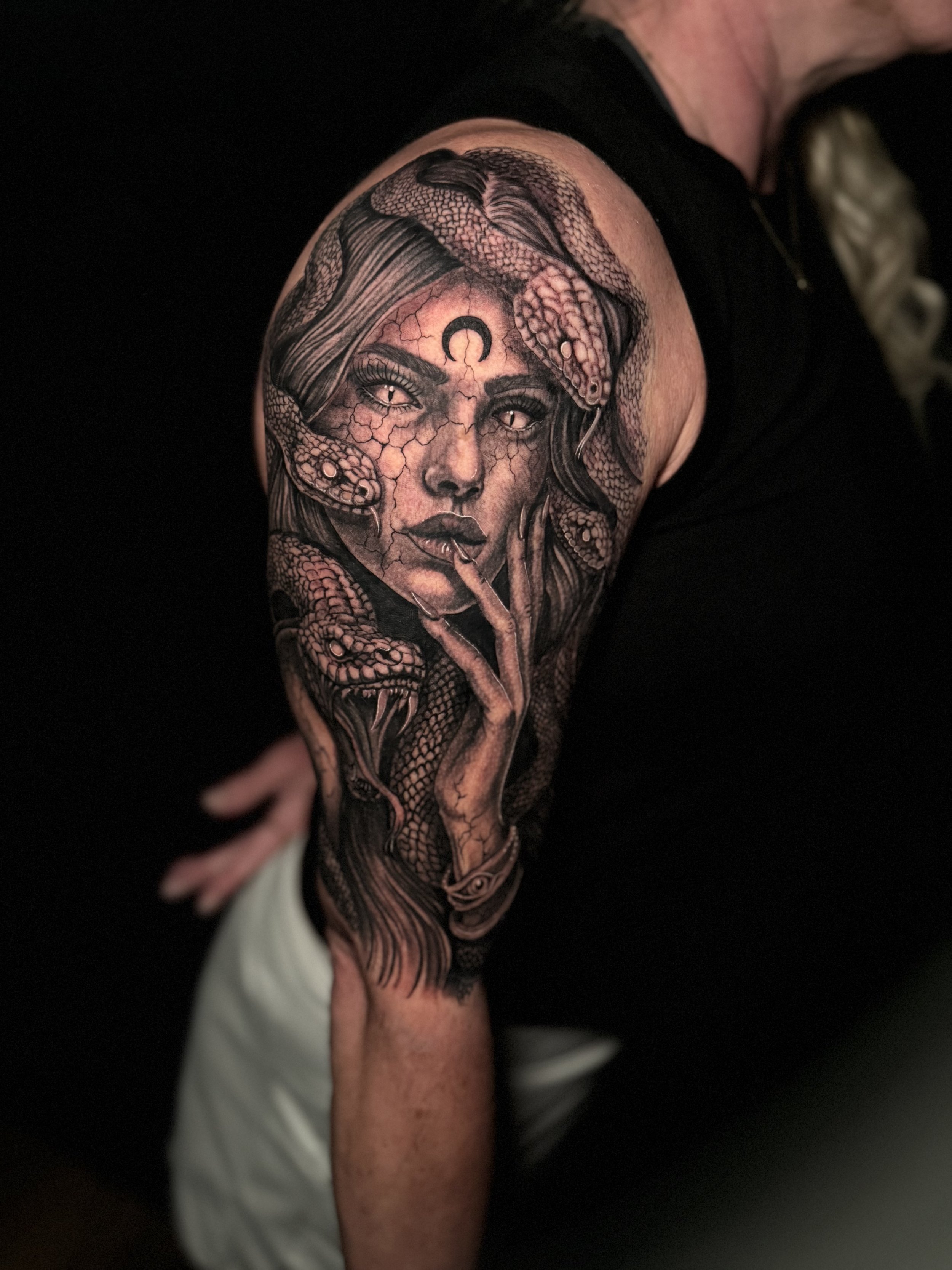 Tattoo of a woman's face with a large snake surrounding her head and shoulders on a person's arm.