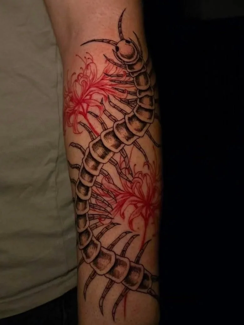 Tattoo of a black and gray scorpion with red floral accents on a person's arm