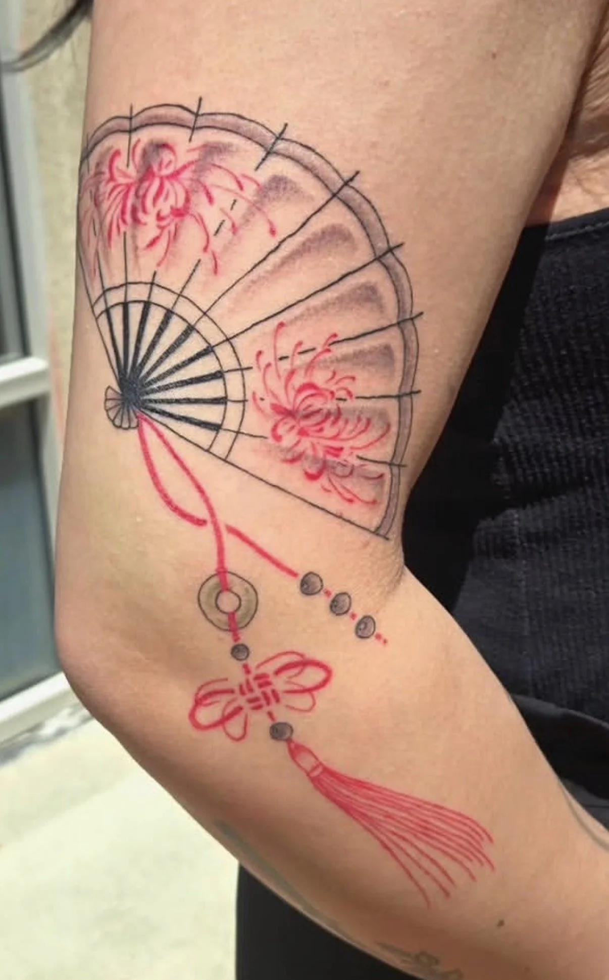 Tattoo of a mechanical fan, red flowers, and a flower with trailing tassels on a person's arm.