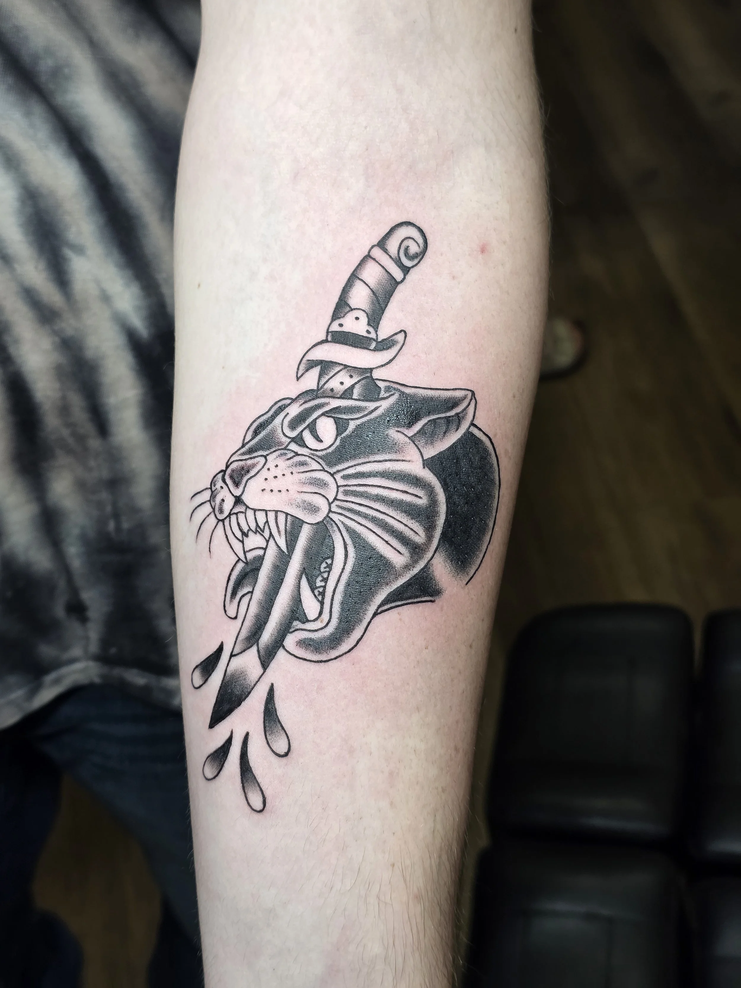 Tattoo of a panther's head with a sword through it on a person's forearm.