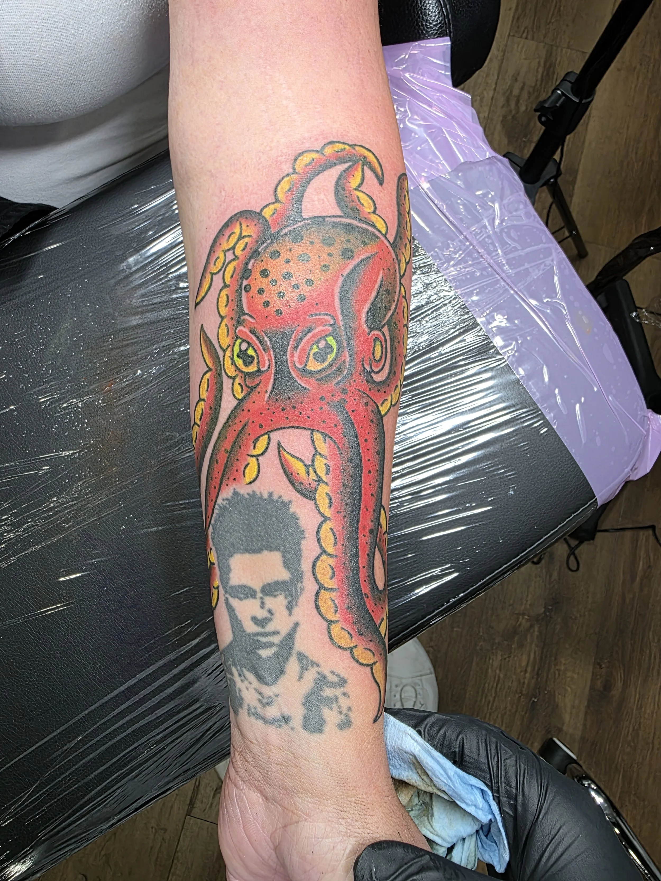 A colorful tattoo of a squid with a woman’s face shown on a person's forearm.