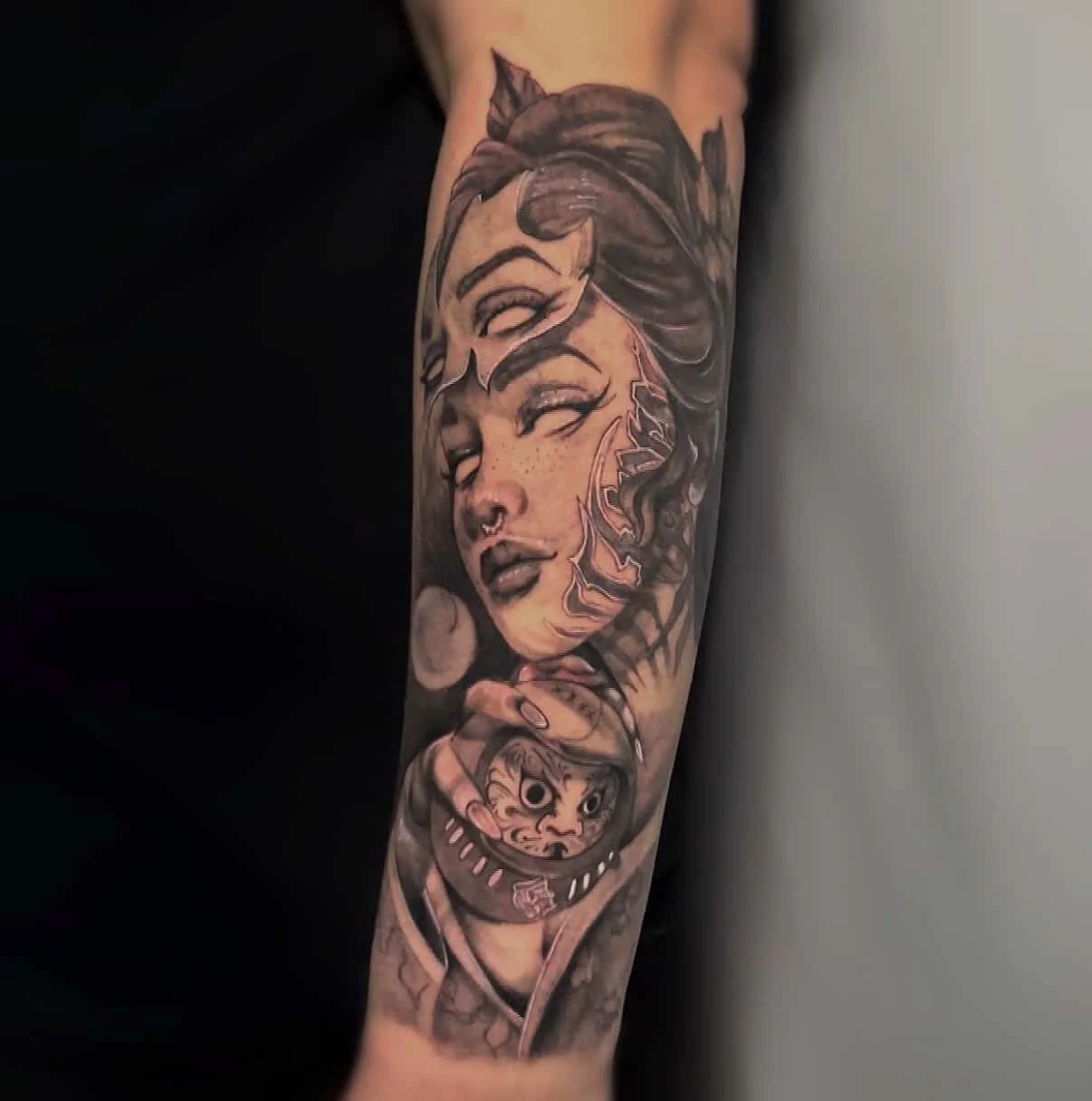 Tattoo of a woman's face with cat ears, freckles, and a nose ring, along with a face with a hat, on a person's arm.