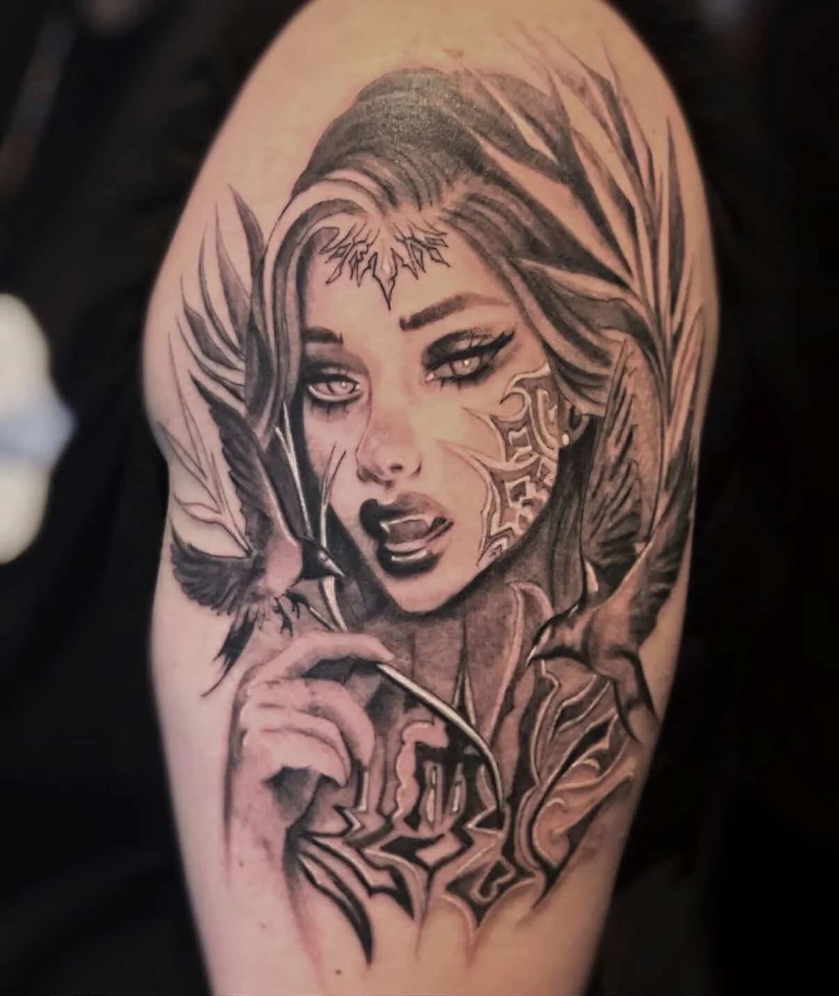 Tattoo of a woman with long hair, intense eyes, and makeup. She is holding a feather with a bird, surrounded by feathers and intricate designs.