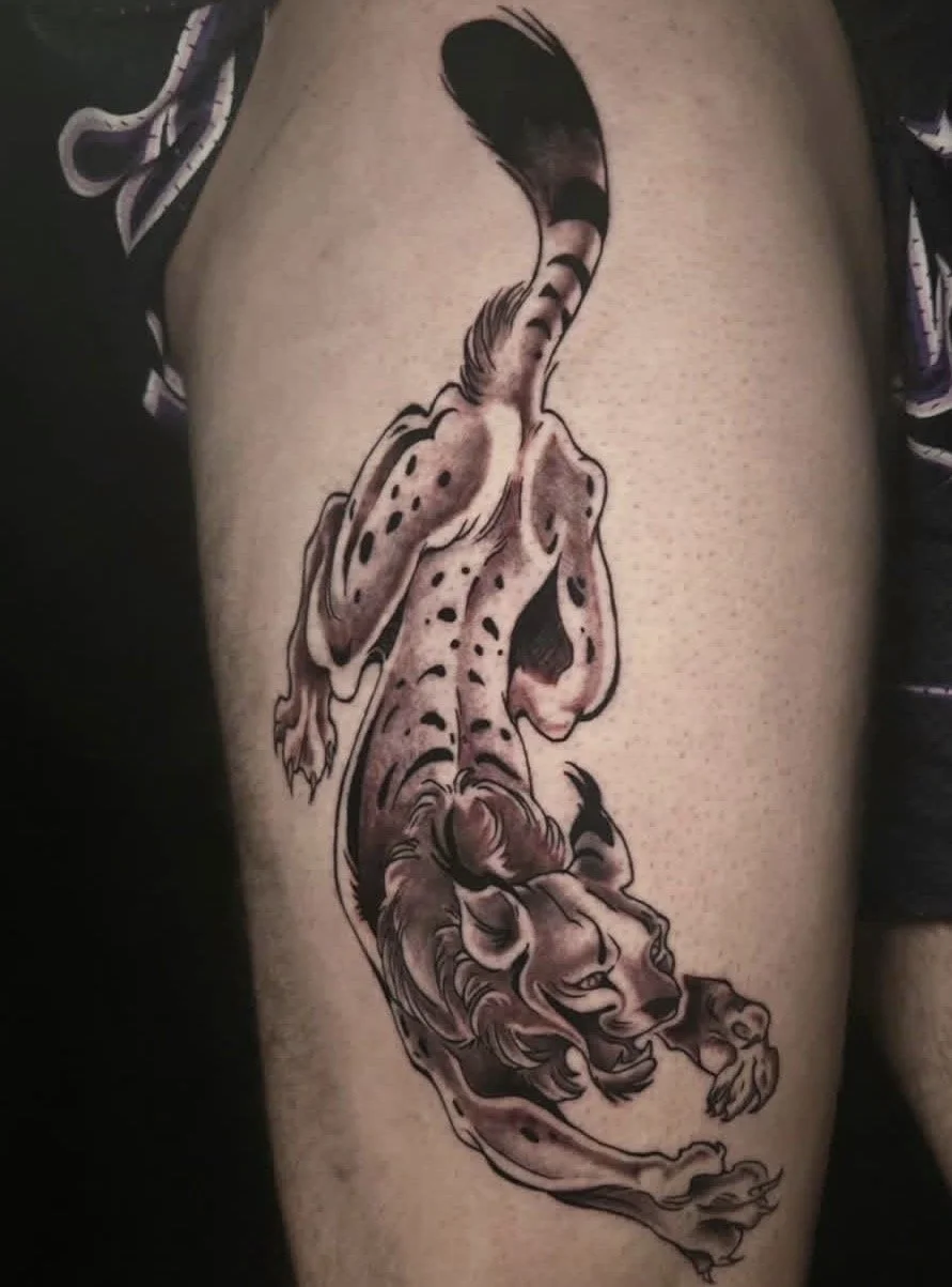 Tattoo of a curled feline, resembling a cheetah or leopard, with stylized design on person's thigh.