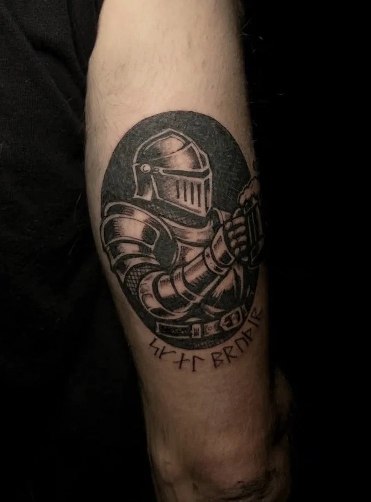 Tattoo of a knight in armor holding a small object, with runic or ancient script underneath.