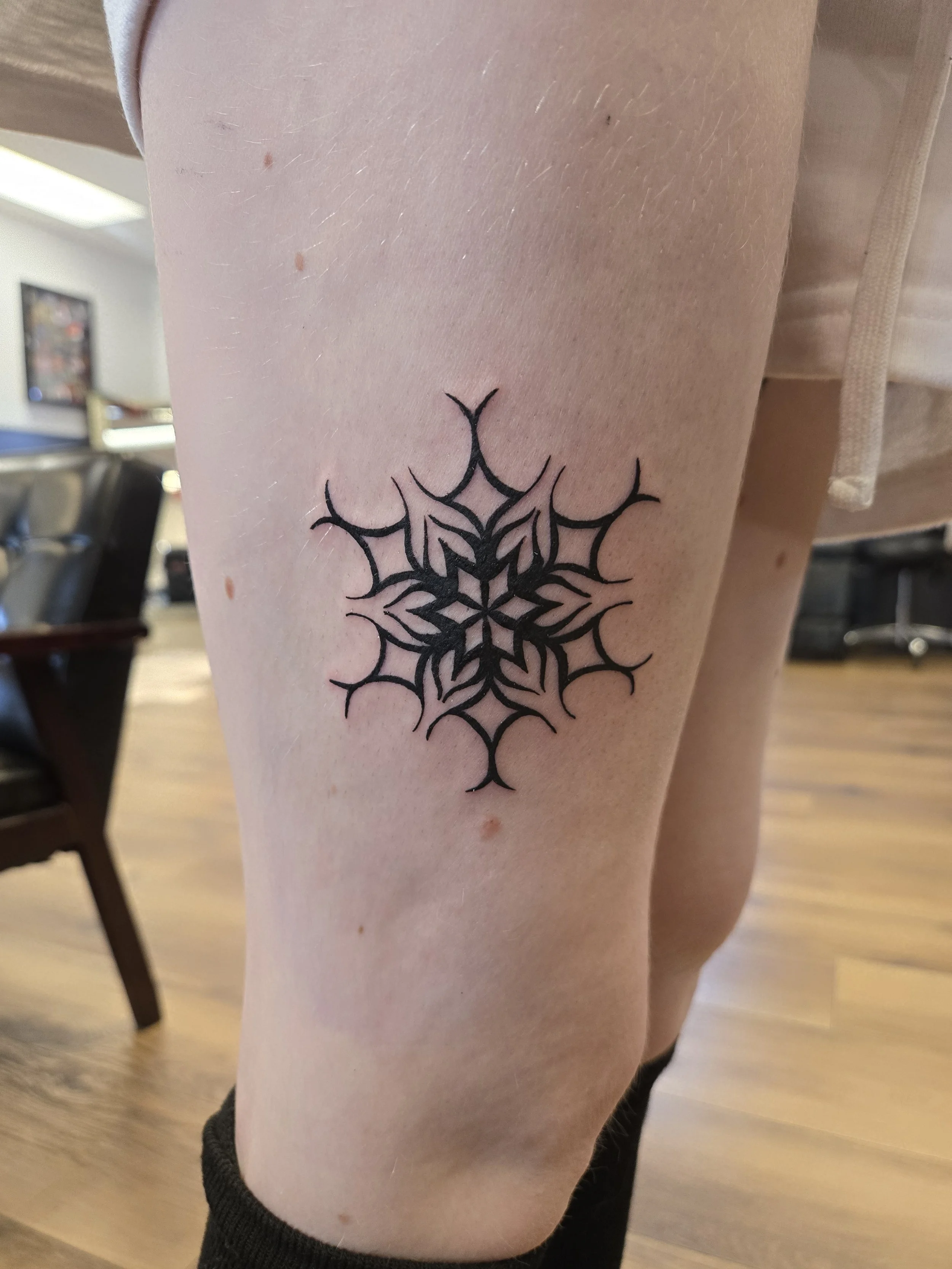 A person's upper arm with a detailed black tattoo of a geometric spider web design.