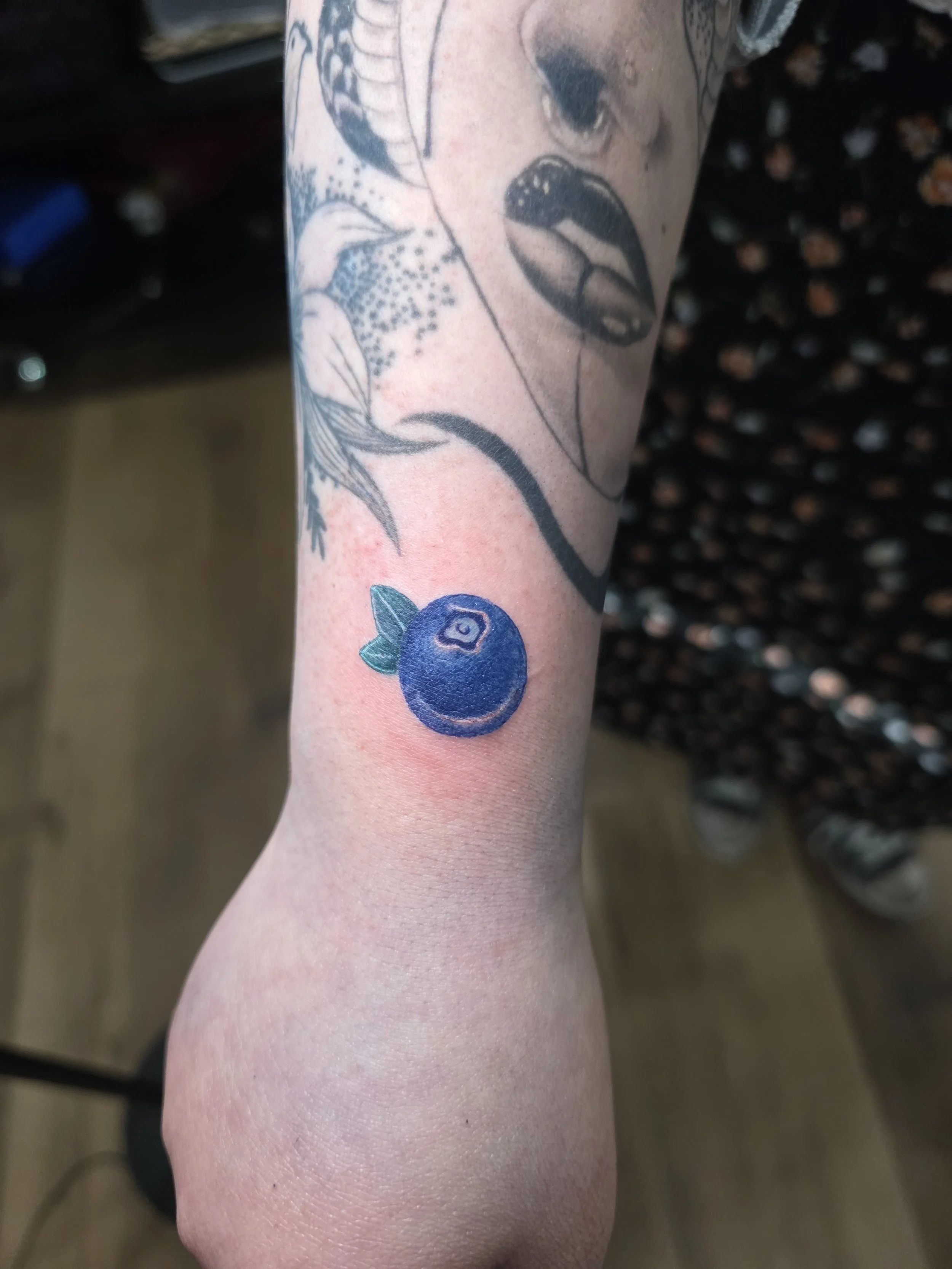 Tattoo of a blue berry and a bird on a person's arm.