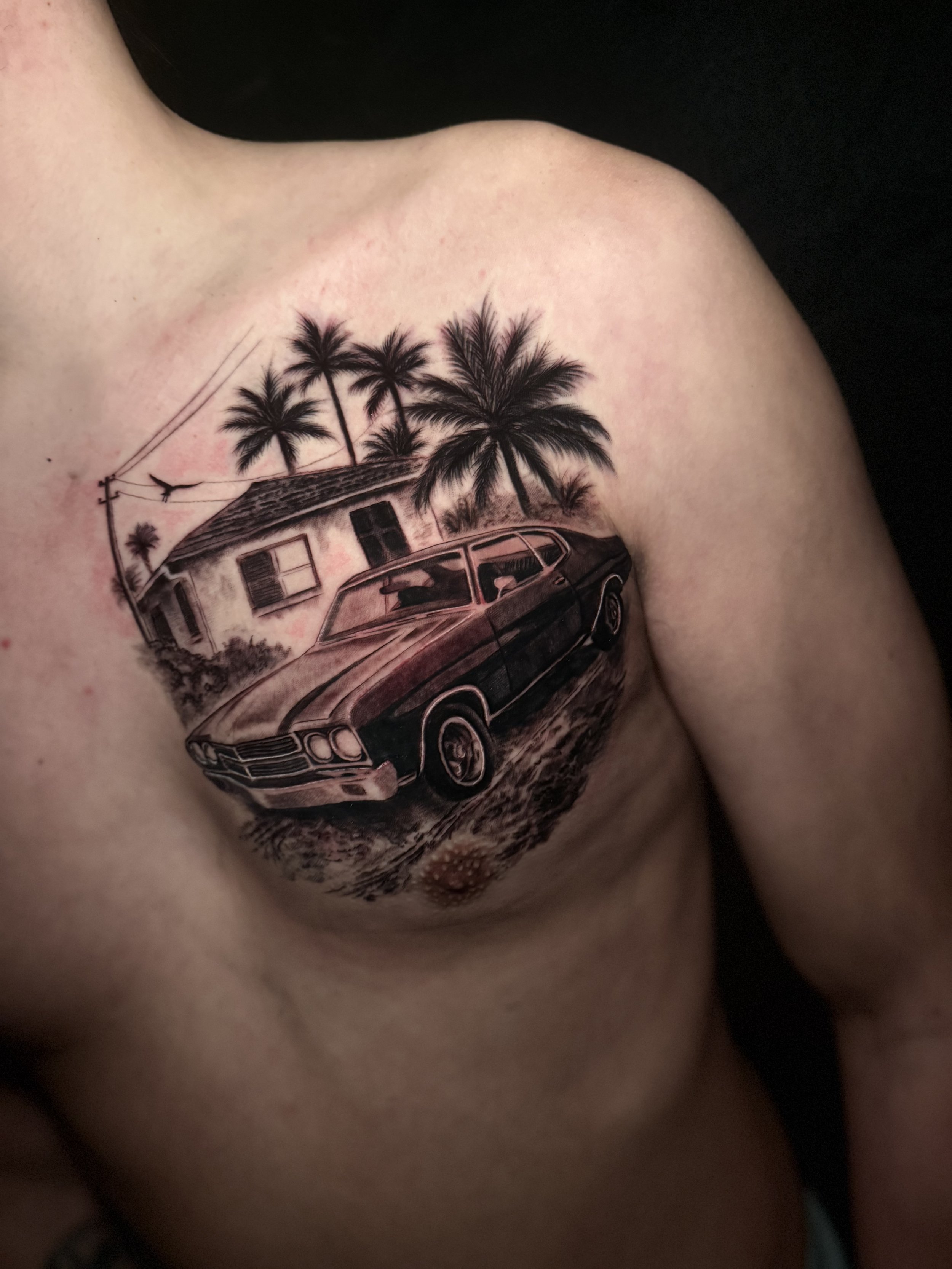 A tattoo on a person's chest depicting palm trees, a house, and a vintage car.
