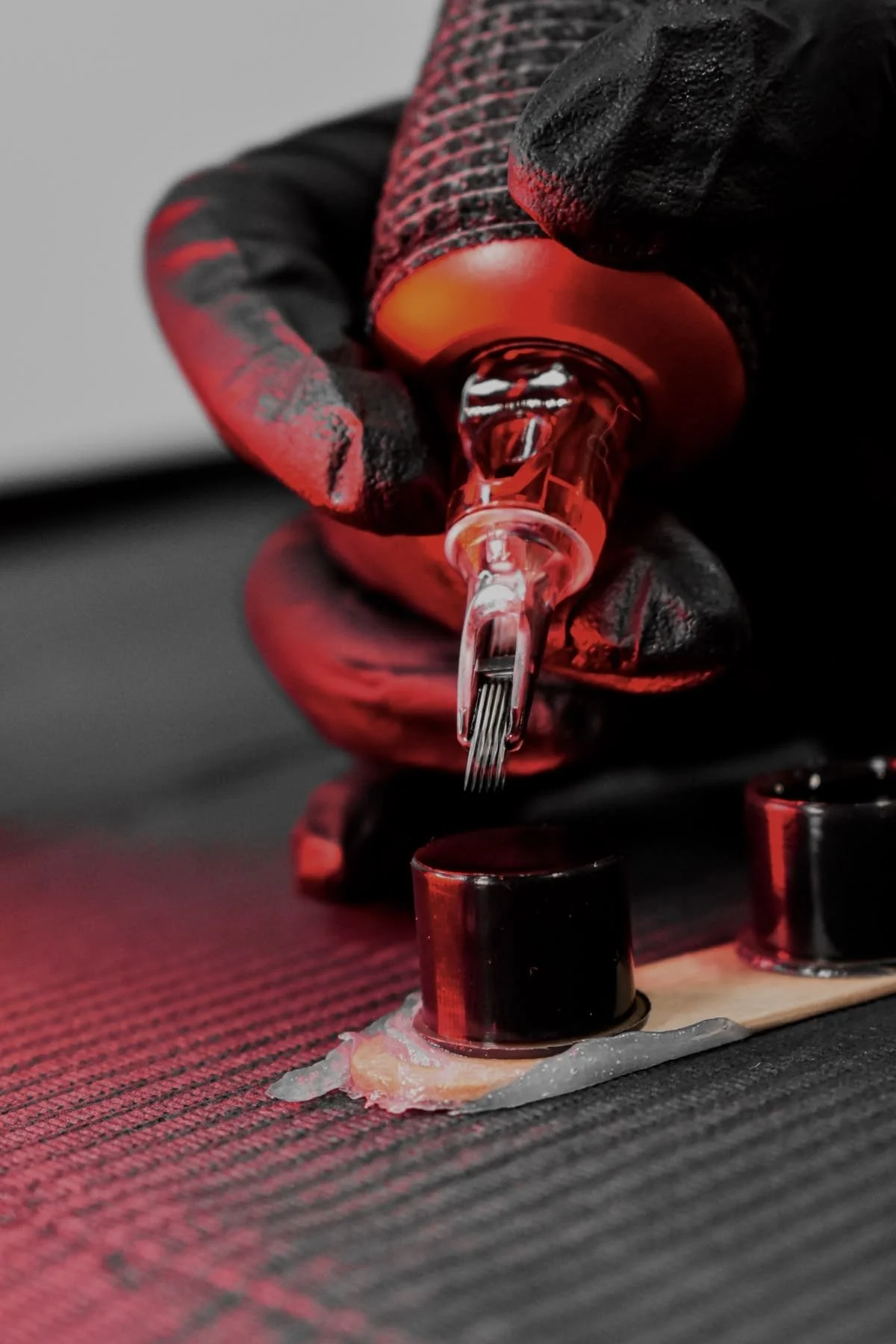 Close-up of a tattoo artist's hand in black and red gloves holding a tattoo machine with red light, tattooing black ink onto a person's skin.