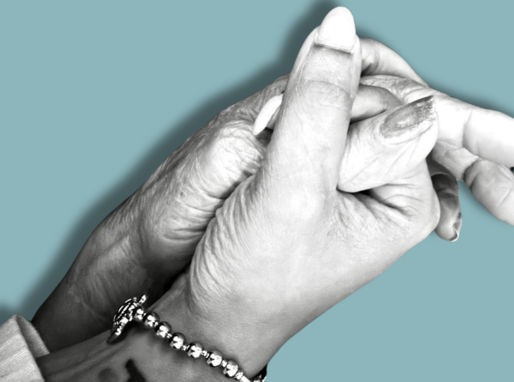 Close-up of two hands, one younger and one older, clasped together against a plain blue background.