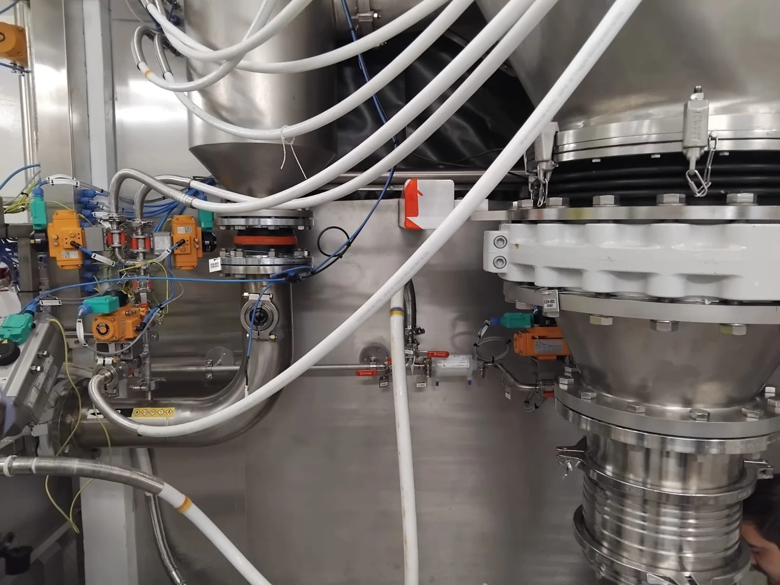 Vue d'une machine industrielle avec des tuyaux, des vannes et des composants métalliques, probablement dans un contexte de fabrication ou de laboratoire.