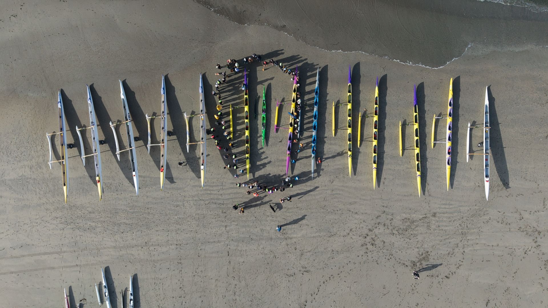 An aerial view of a beach with kayaks forming the word 'LOVE' and people gathered in the center, near the shoreline.
