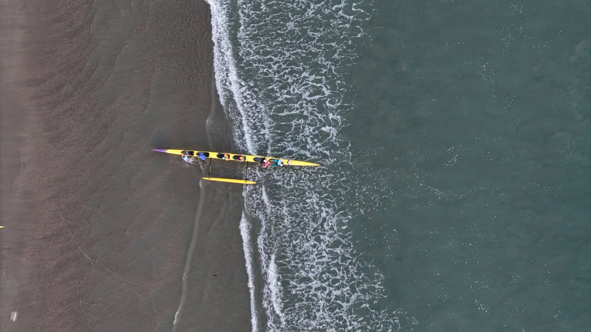 Aerial view of four people on a yellow kayak near the beach shoreline with waves crashing on the sand.