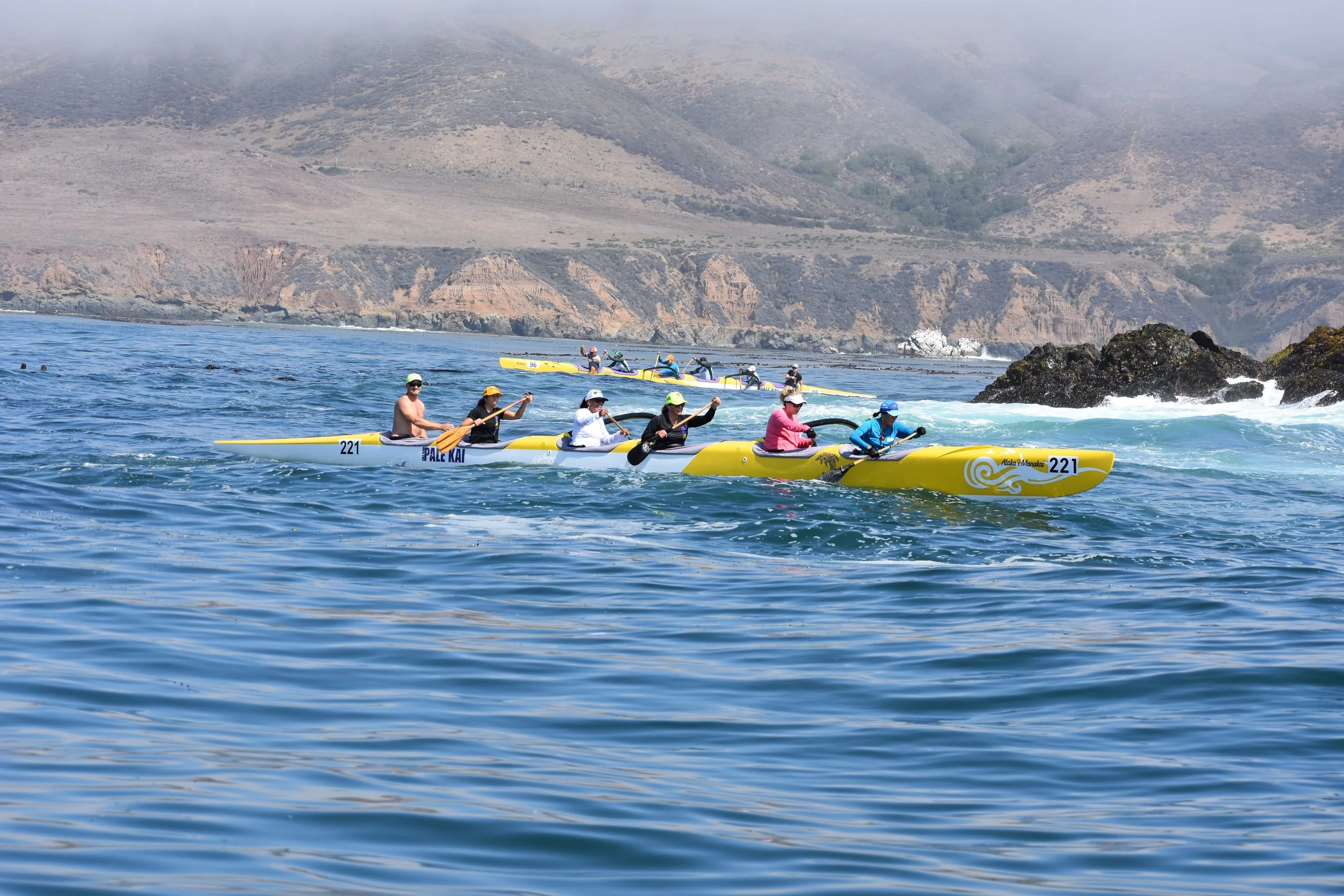 People kayaking in the ocean with mountains in the background.
