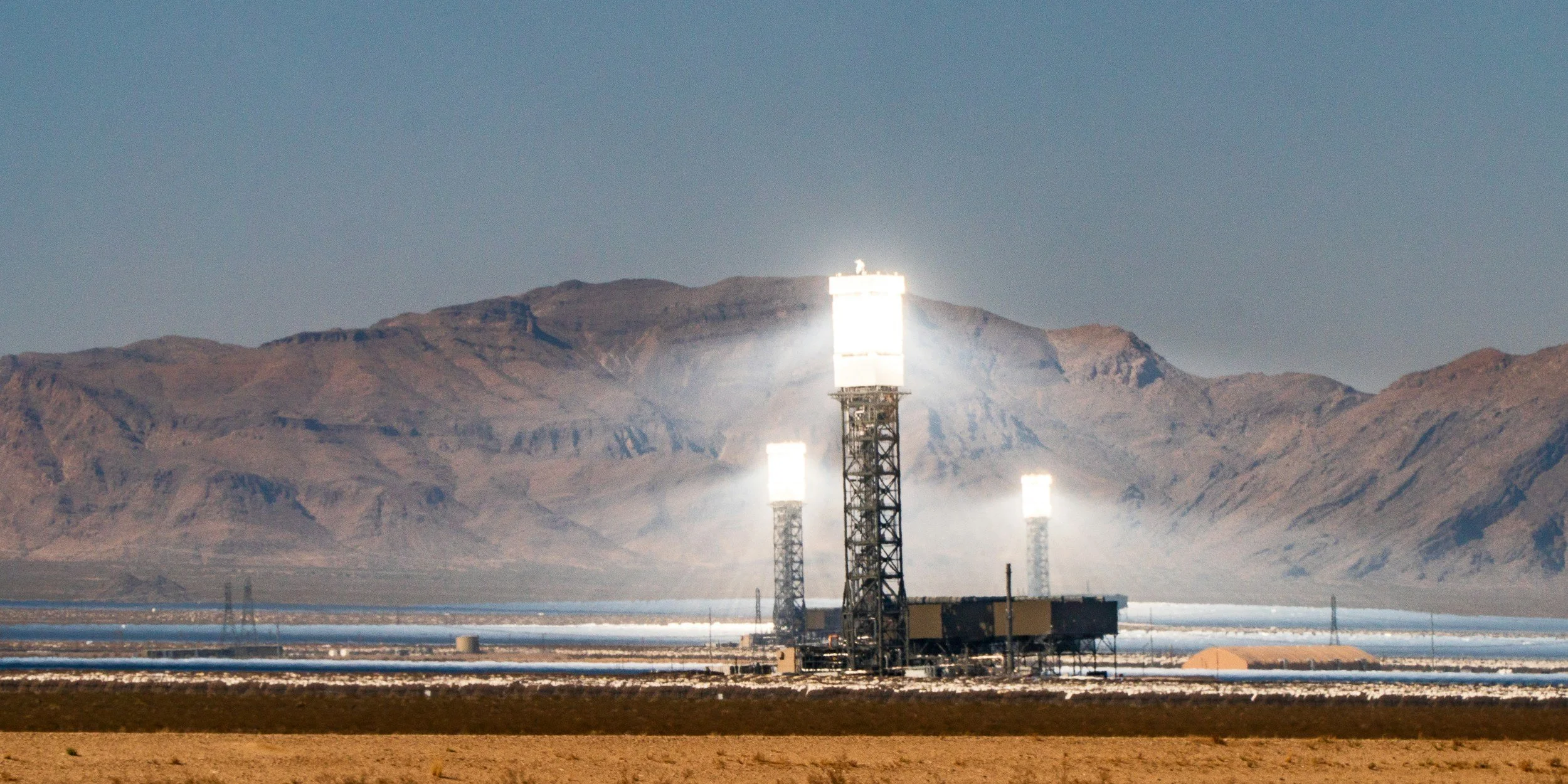 Desert landscape with mountains in the background and tall communication towers with white tops in the foreground.
