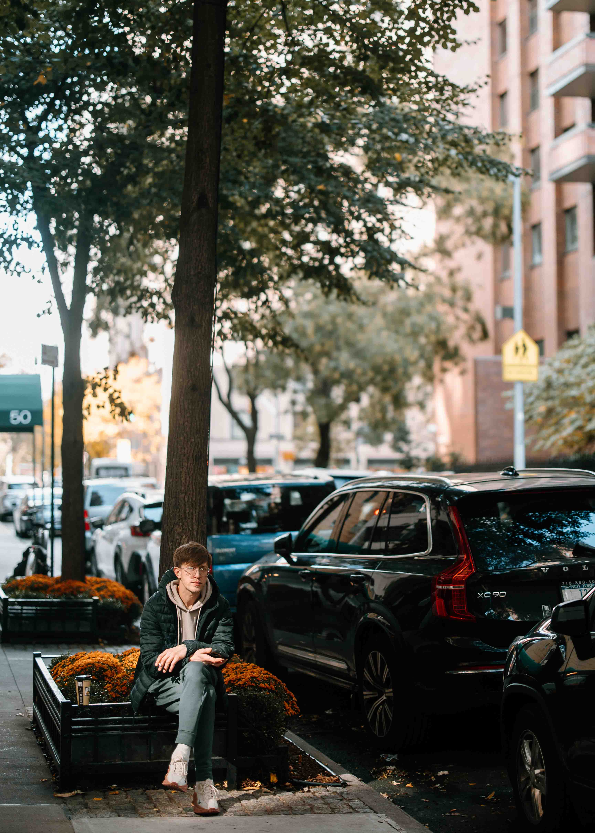 Lifestyle photograph of a young man sitting on a park bench with orange flowers and a drink in an urban neighborhood.
