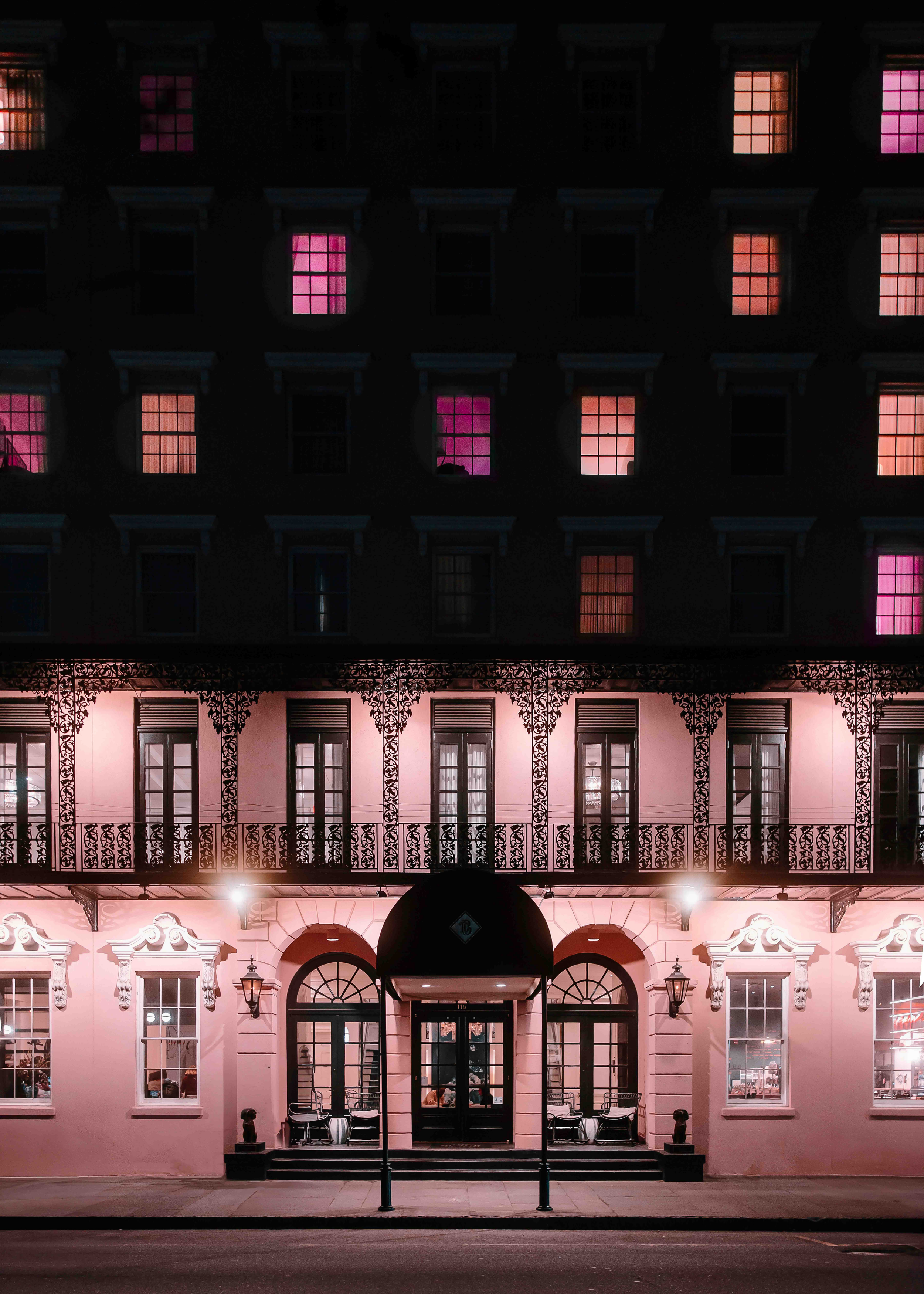 Architectural photograph of a historic building at night with glowing pink and orange windows and ornate wrought iron balconies.