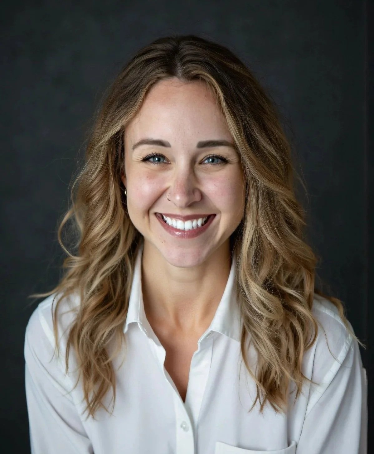 Portrait of a smiling woman with wavy light brown hair, wearing a white collared shirt, against a dark background.