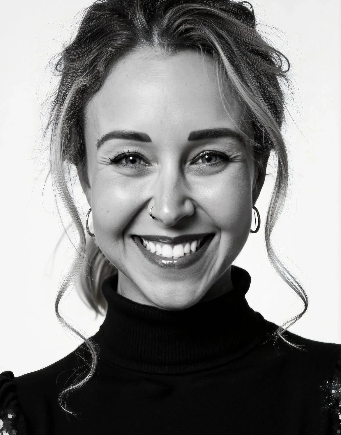 Black and white portrait of a smiling woman with wavy hair, hoop earrings, and a turtleneck top.