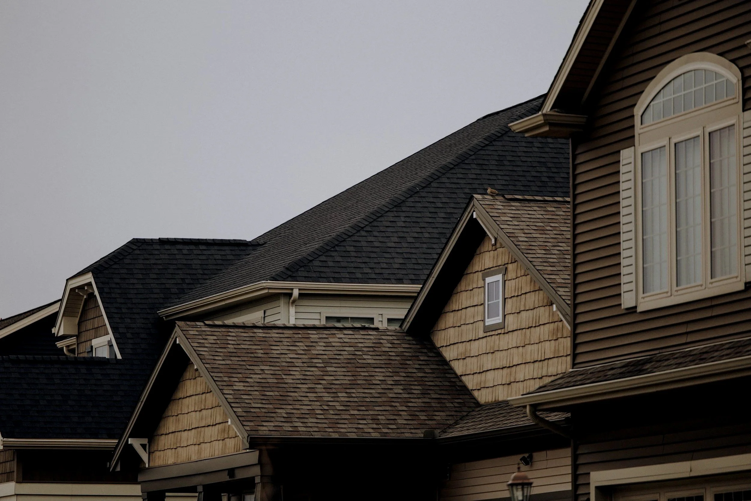 Close-up of houses with peaked roofs, shingles, and windows, under an overcast sky.