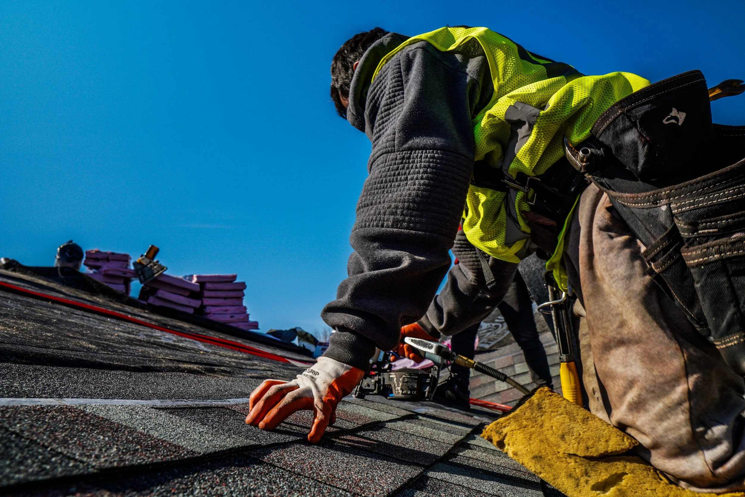 Worker installing roof shingles on a house under a clear blue sky.