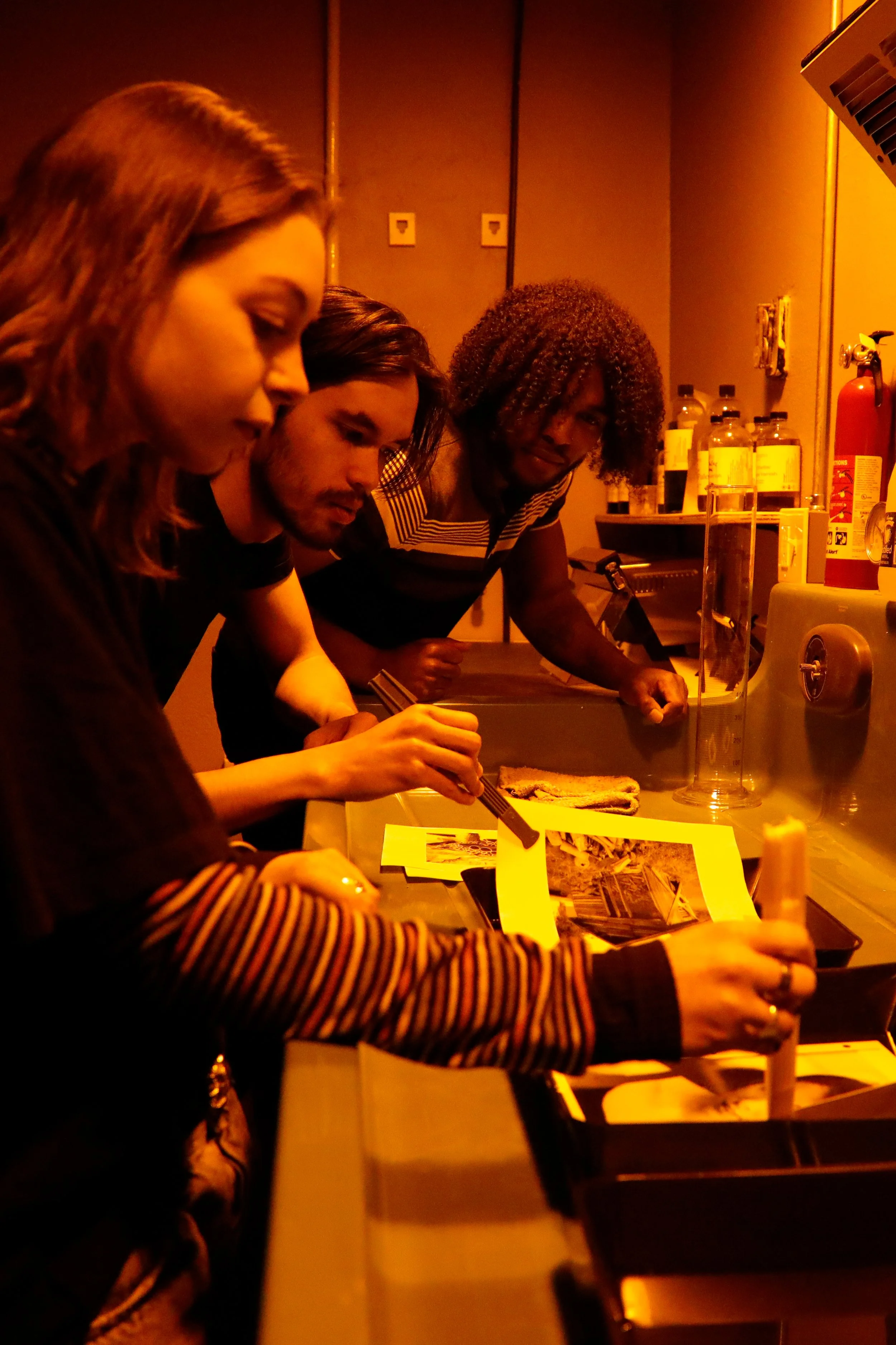 At a rentable darkroom in Niagara Falls NY, Three people at a photo darkroom sink engaged in developing a photo.