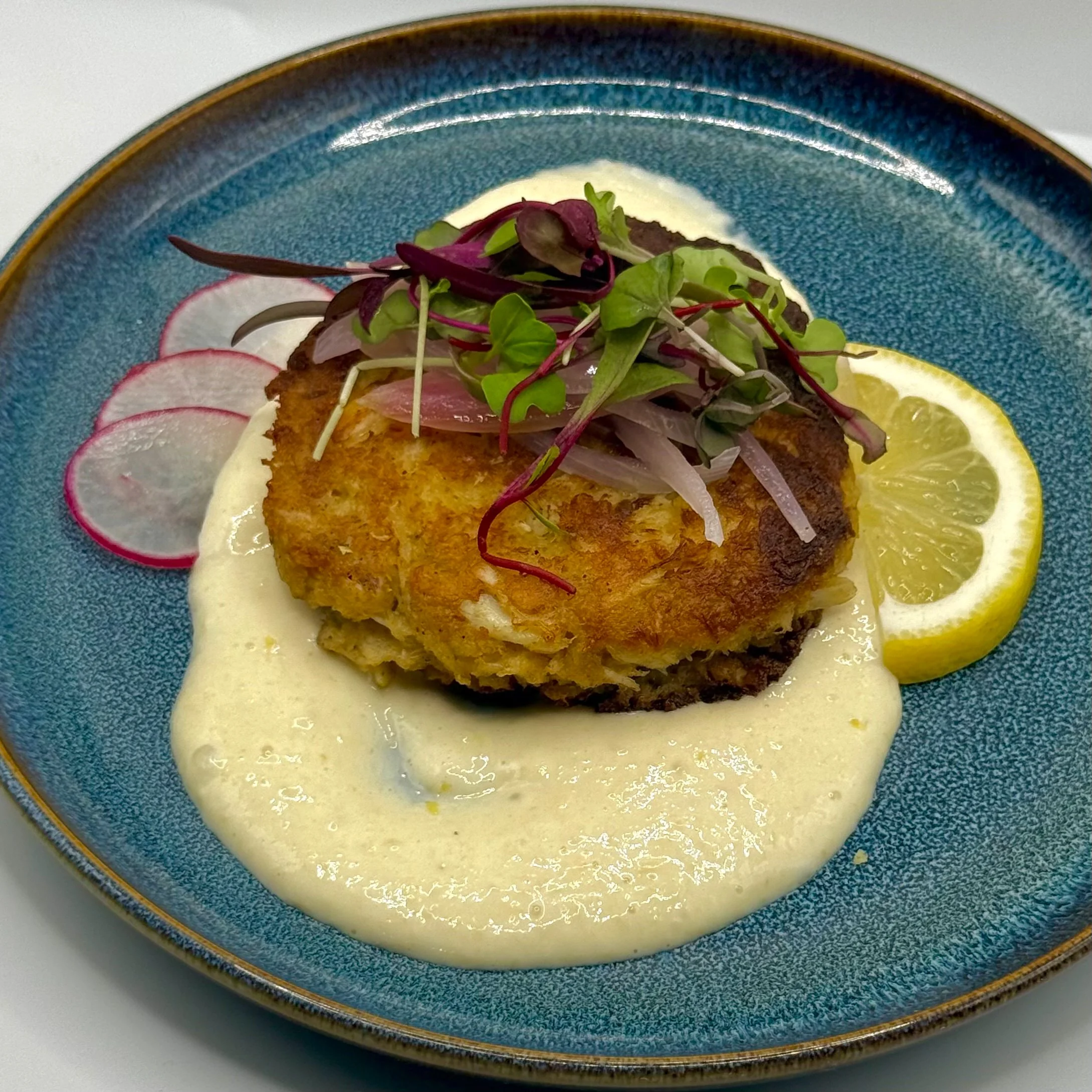 Golden, tender Jumbo Lump Crab Cake perched over a silky lemon-garlic horseradish sauce, crowned with bright pickled red onions and peppery micro-radish for a luxurious, flavor-packed bite. 