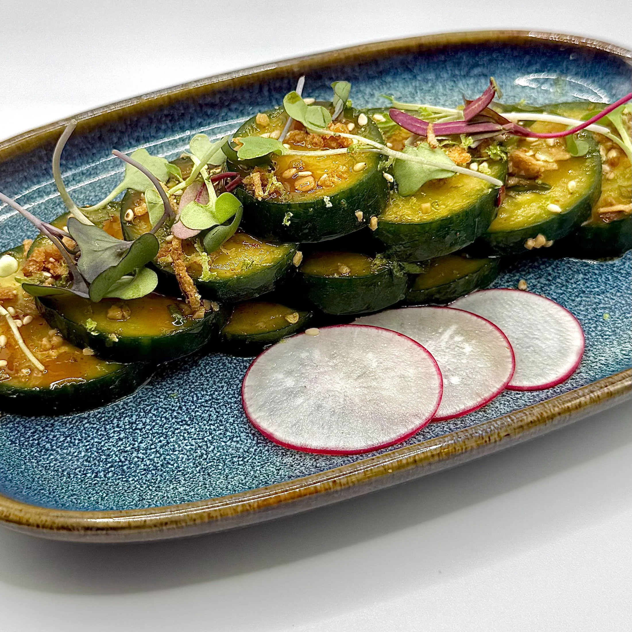 Thick-cut cucumber coins tossed in a spicy garlic ponzu sauce. Topped with sesame seeds, crispy aromatics, and fresh micro-greens, served alongside thinly shaved radish rounds.