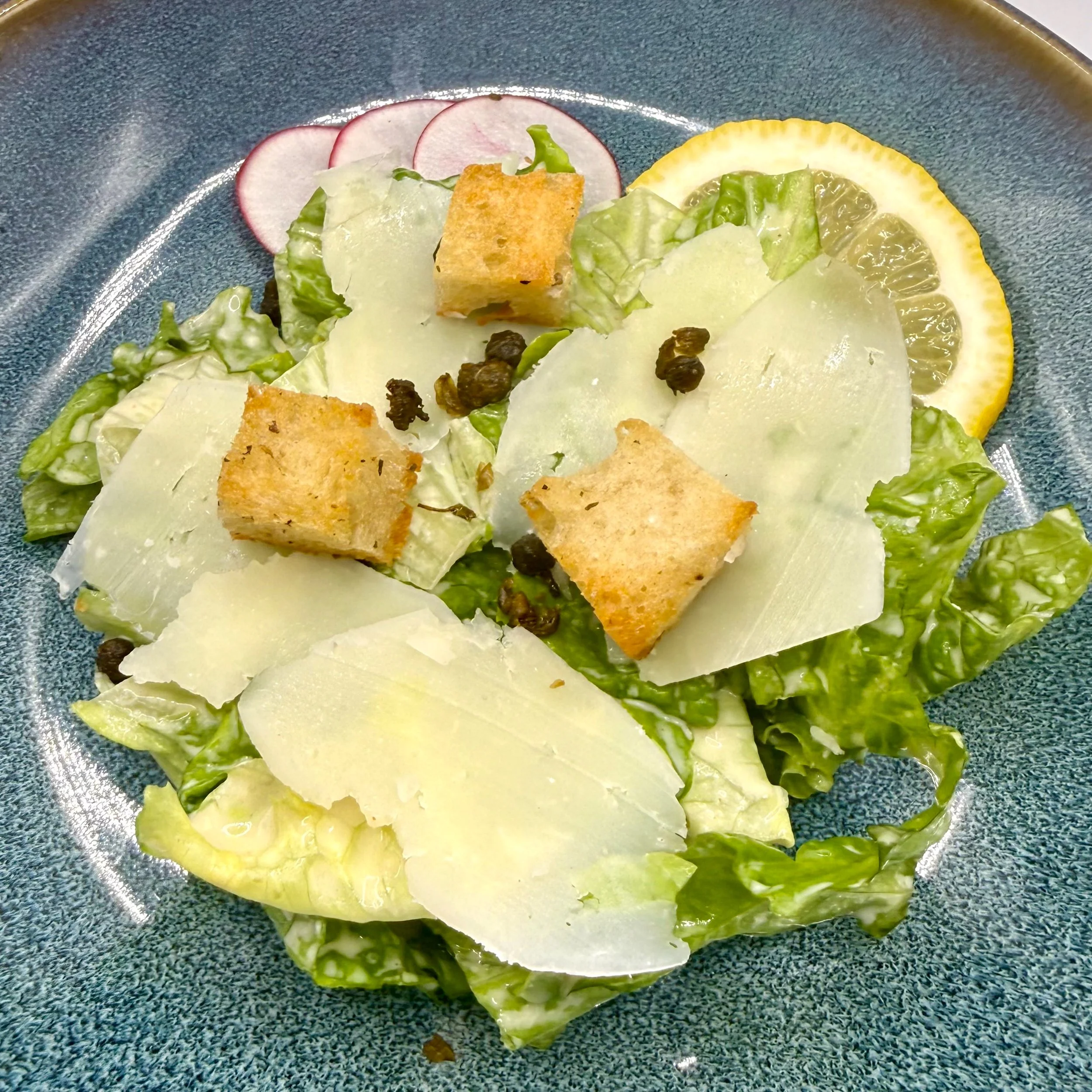 Crisp romaine hearts lightly dressed in Caesar Dressing and draped with thick-cut shavings of aged Parmesan. Topped with golden, toasted croutons and crispy capers for a perfect balance.