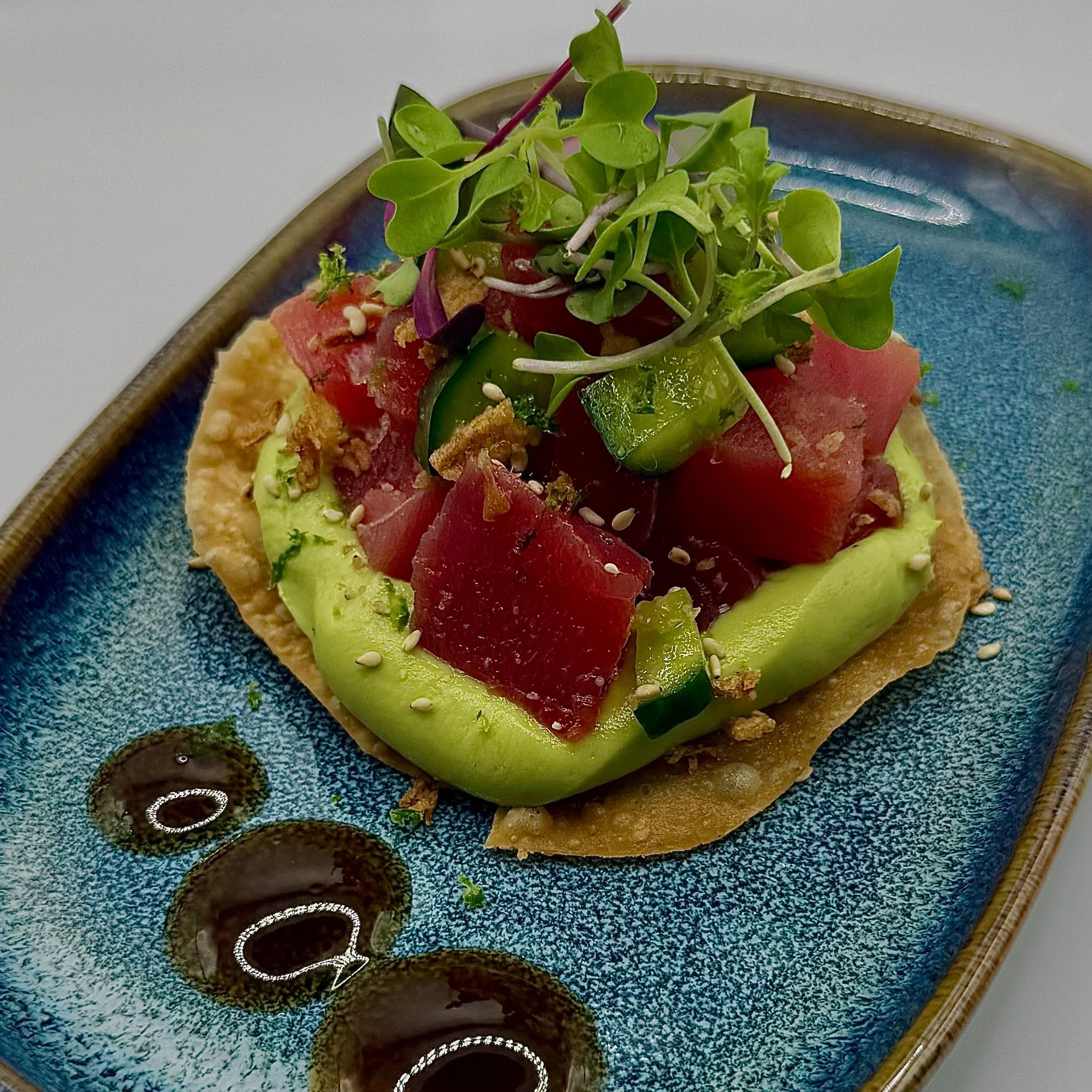 Ahi Tuna Tostada topped with a silky avocado puree, hand-diced tuna, and crisp cucumbers. Finished with toasted sesame seeds, fresh micro-greens, and a savory yuzu gel for a perfectly balanced bite.