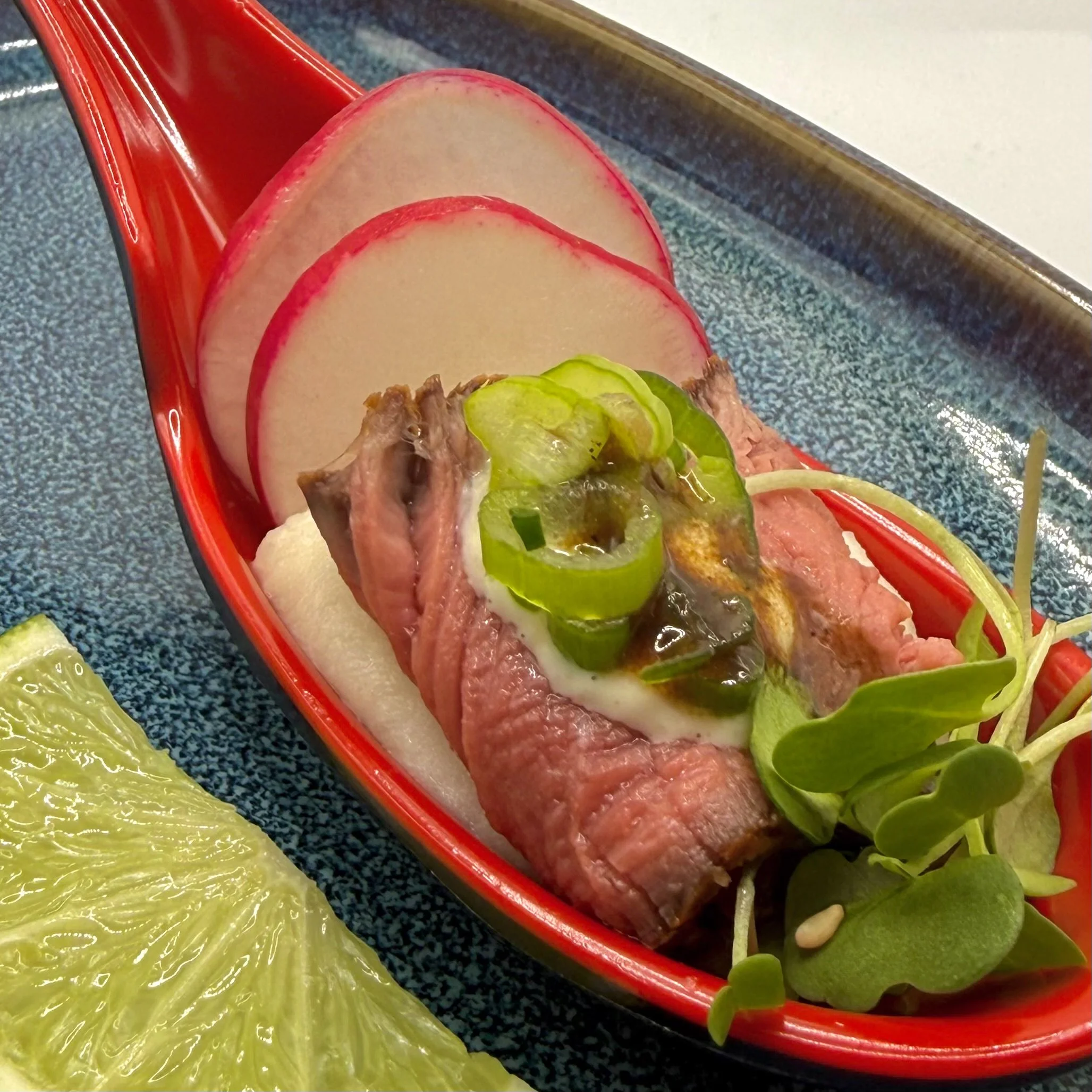 A tender, pan-seared Filet Mignon medallion served medium-rare over a velvety garlic potato puree. Nestled in a tasting spoon with a crisp radish round and fresh micro-greens