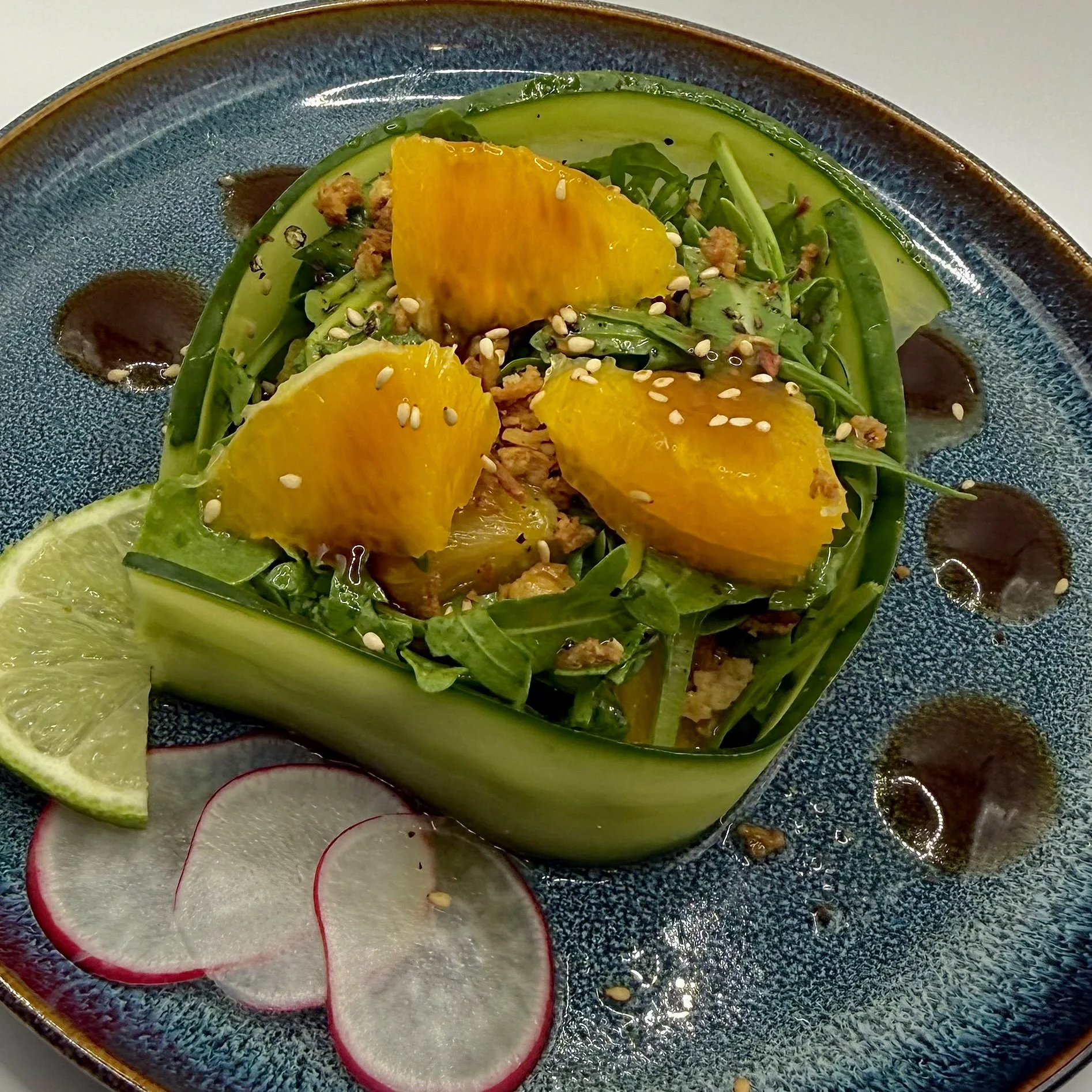 Cucumber Wrapped Citrus Salad featuring fresh arugula and bright orange segments, all encased in a crisp cucumber ribbon. Finished with toasted sesame seeds and thin radish rounds for a refreshing, high-contrast bite.