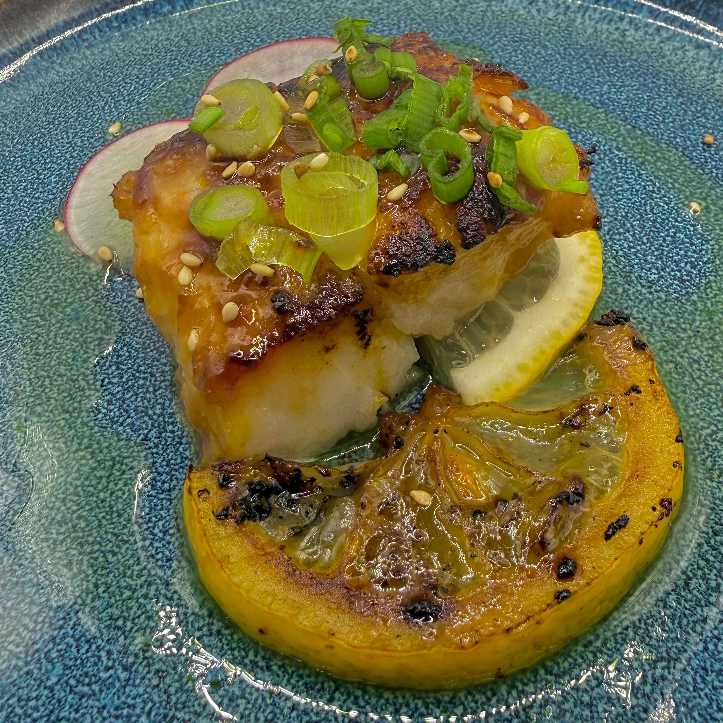 Atlantic Cod cured for 24 hours in a traditional miso-mirin glaze, pan-seared to achieve a deep, caramelized finish. Served with toasted sesame, fresh scallion curls, and a charred lemon wheel for a smoky-citrus edge.