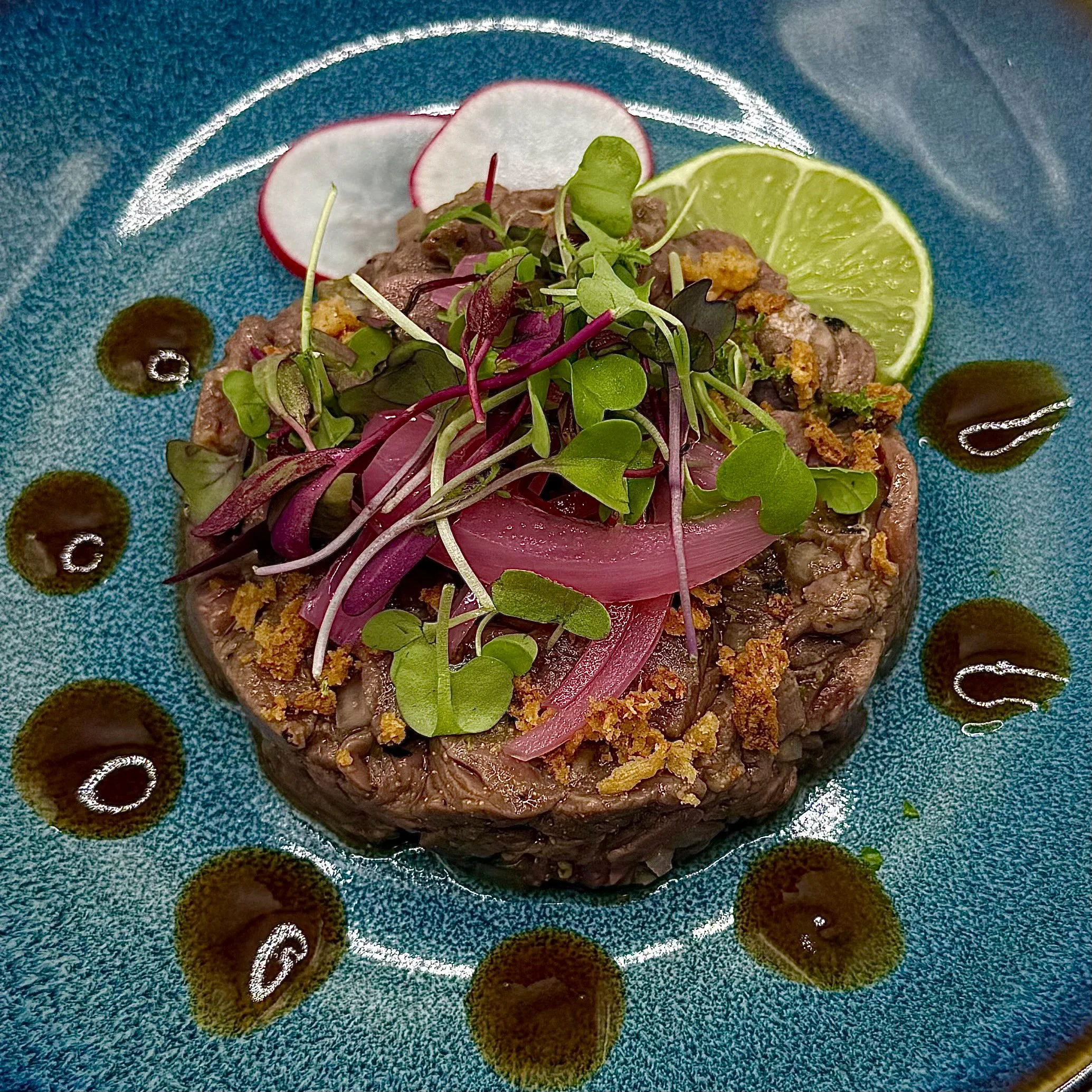 Hand-cut steak tartare topped with pickled red onions, peppery micro-radish, and a toasted garlic crunch. Finished with a fresh lime zing and droplets of yuzu gel.