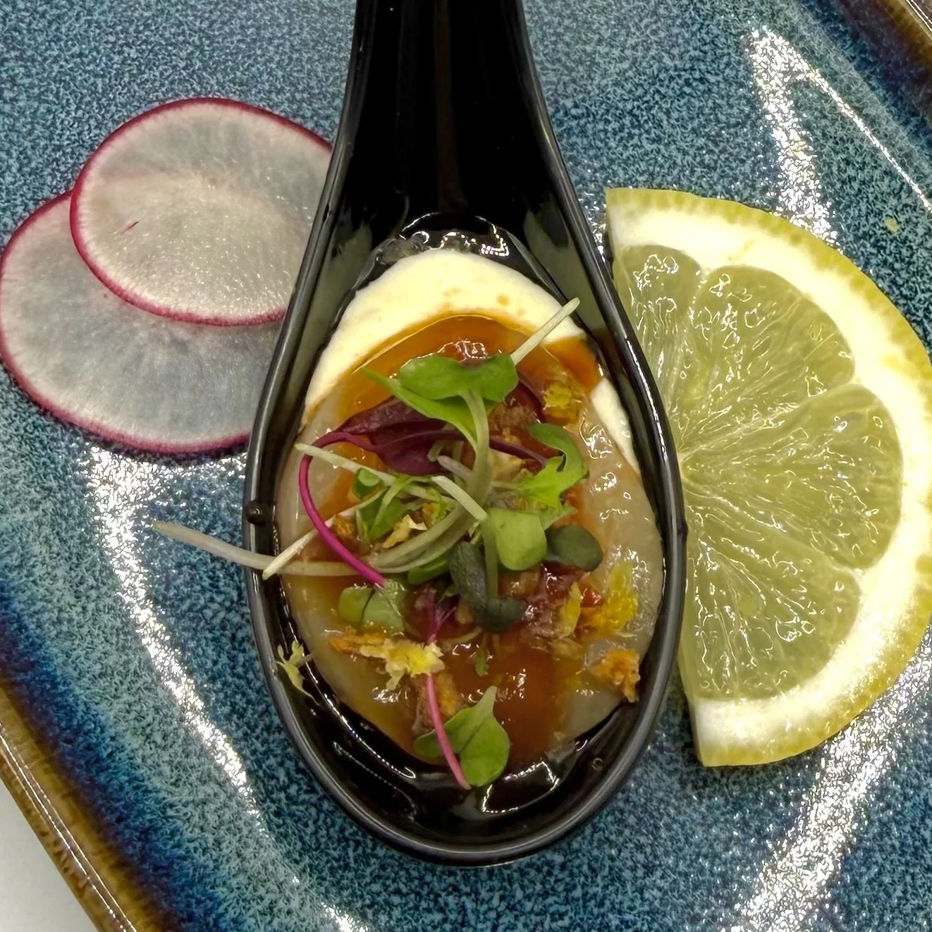 Tender scallop medallion resting on a sharp, creamy horseradish aioli, kissed with a splash of spicy ponzu, toasted garlic crunch, and bright citrus zest—an elegant, flavor-packed one-bite delight. 
