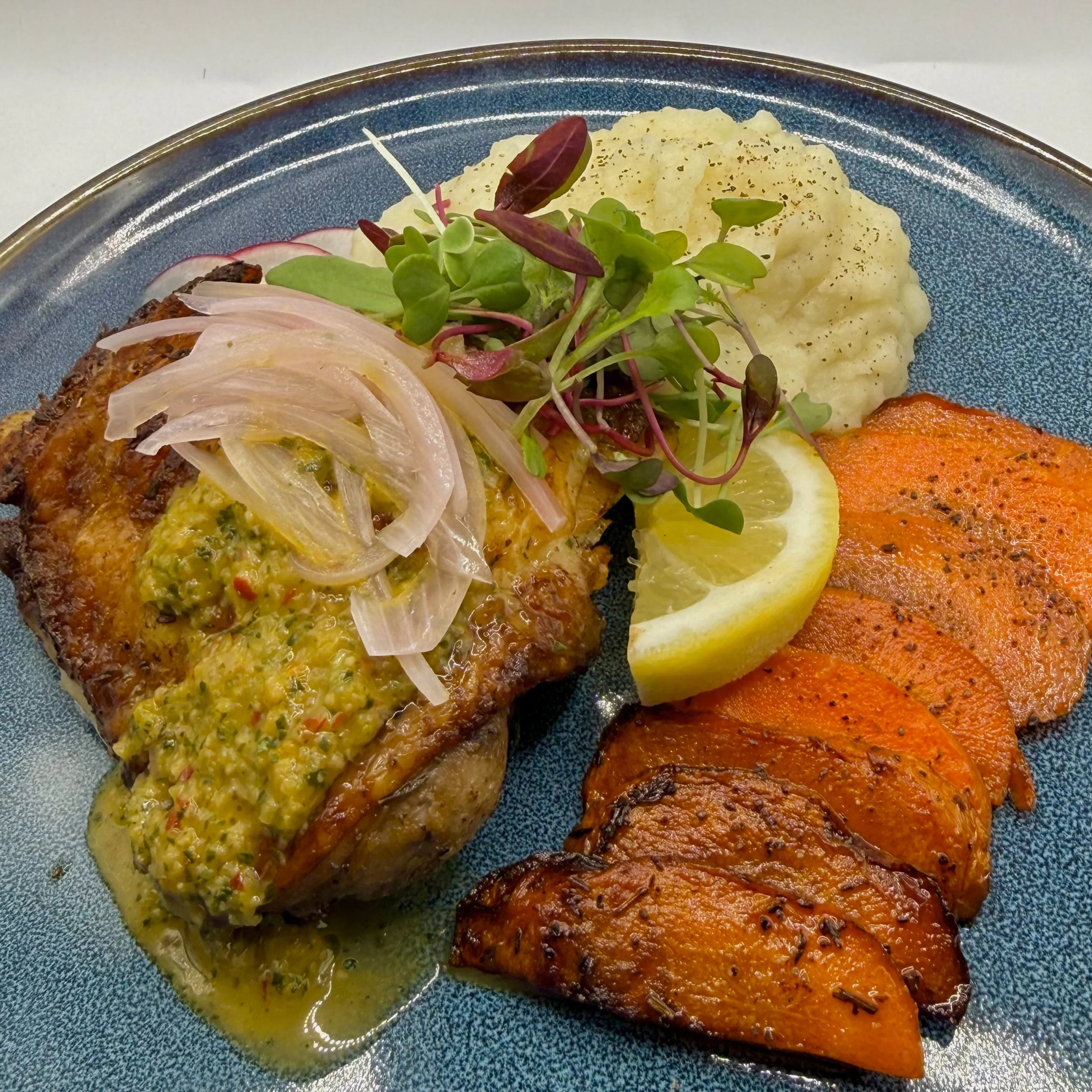 Bone-in, golden Herb Roasted Chicken Thigh served atop velvety garlic mashed potatoes and honey-roasted carrots. Finished with tangy pickled shallots and delicate microgreens for a rustic yet sophisticated presentation.