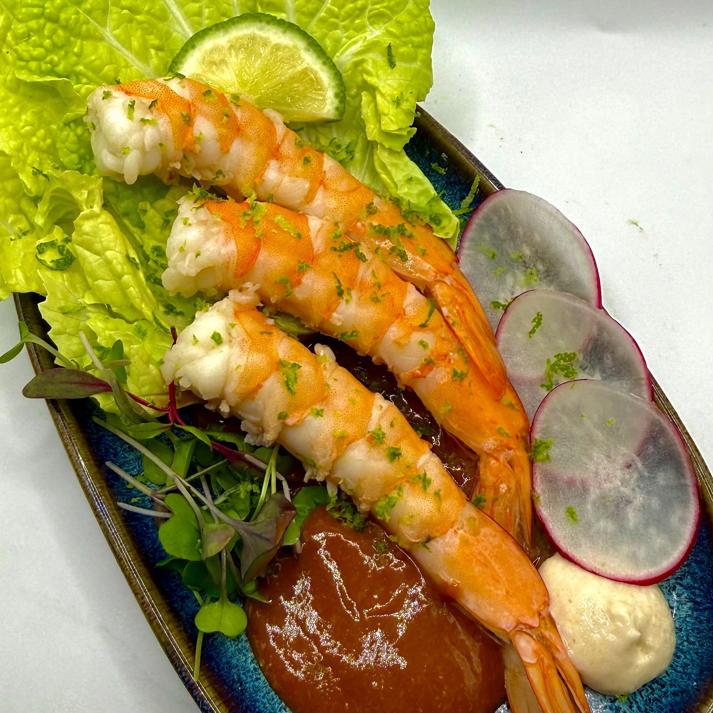 Shrimp Cocktail featuring poached tiger shrimp over crisp leaf lettuce and refreshing radish. Served with a bold, house-made cocktail sauce and a side of horseradish, finished with fresh lime zest for a bright, coastal finish.