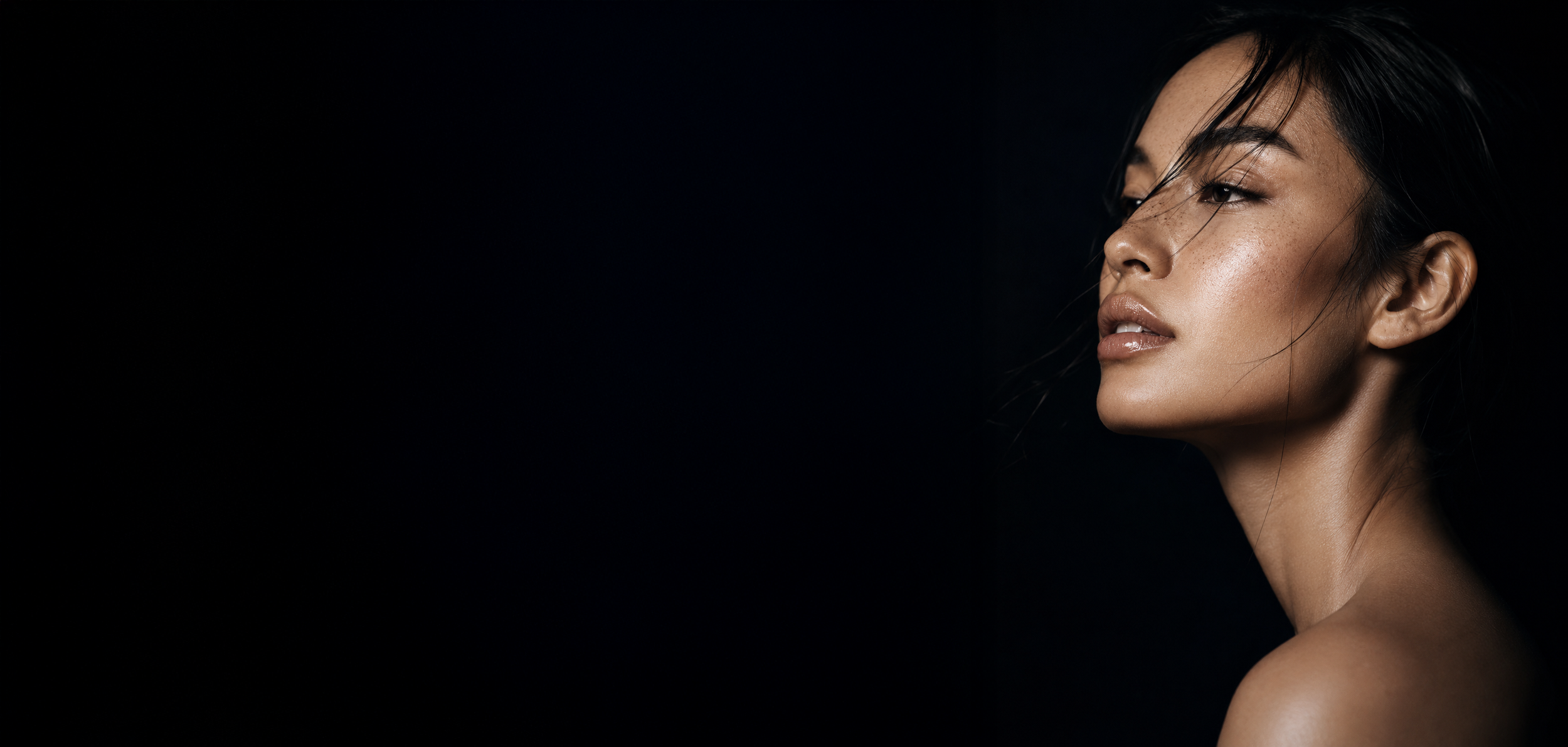 Close-up of a woman with dark hair and natural makeup against a black background.